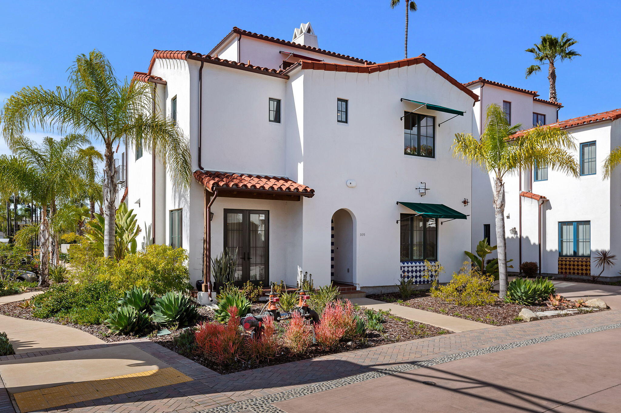 White Spanish-style building with red tile roofs, green awnings, and landscaped gardens around the arched entrance marked 109.