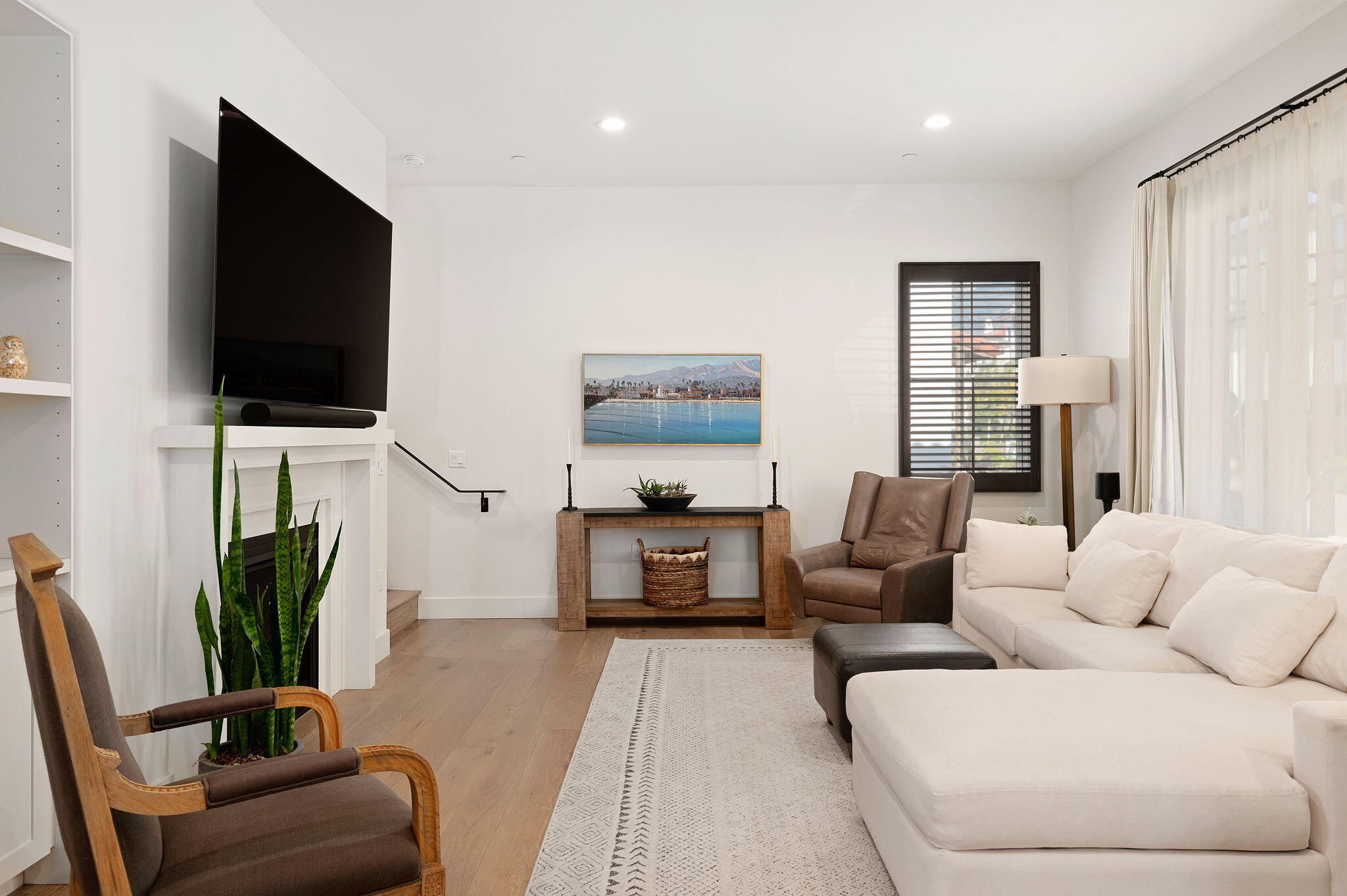 Bright furnished living room with white sectional, fireplace, television, and mountain artwork.