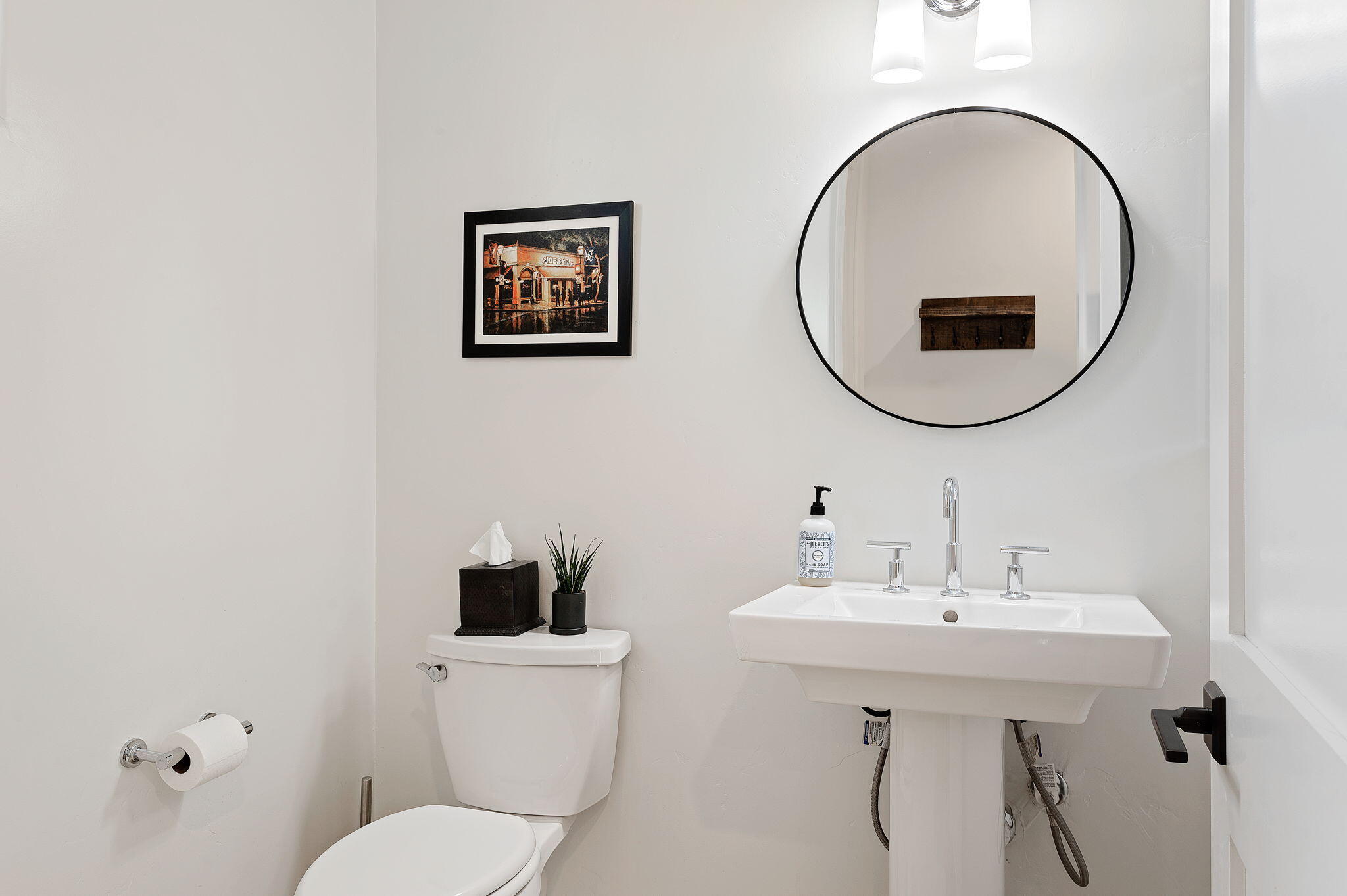 Bathroom with a white pedestal sink, round mirror, chrome fixtures, and toilet.