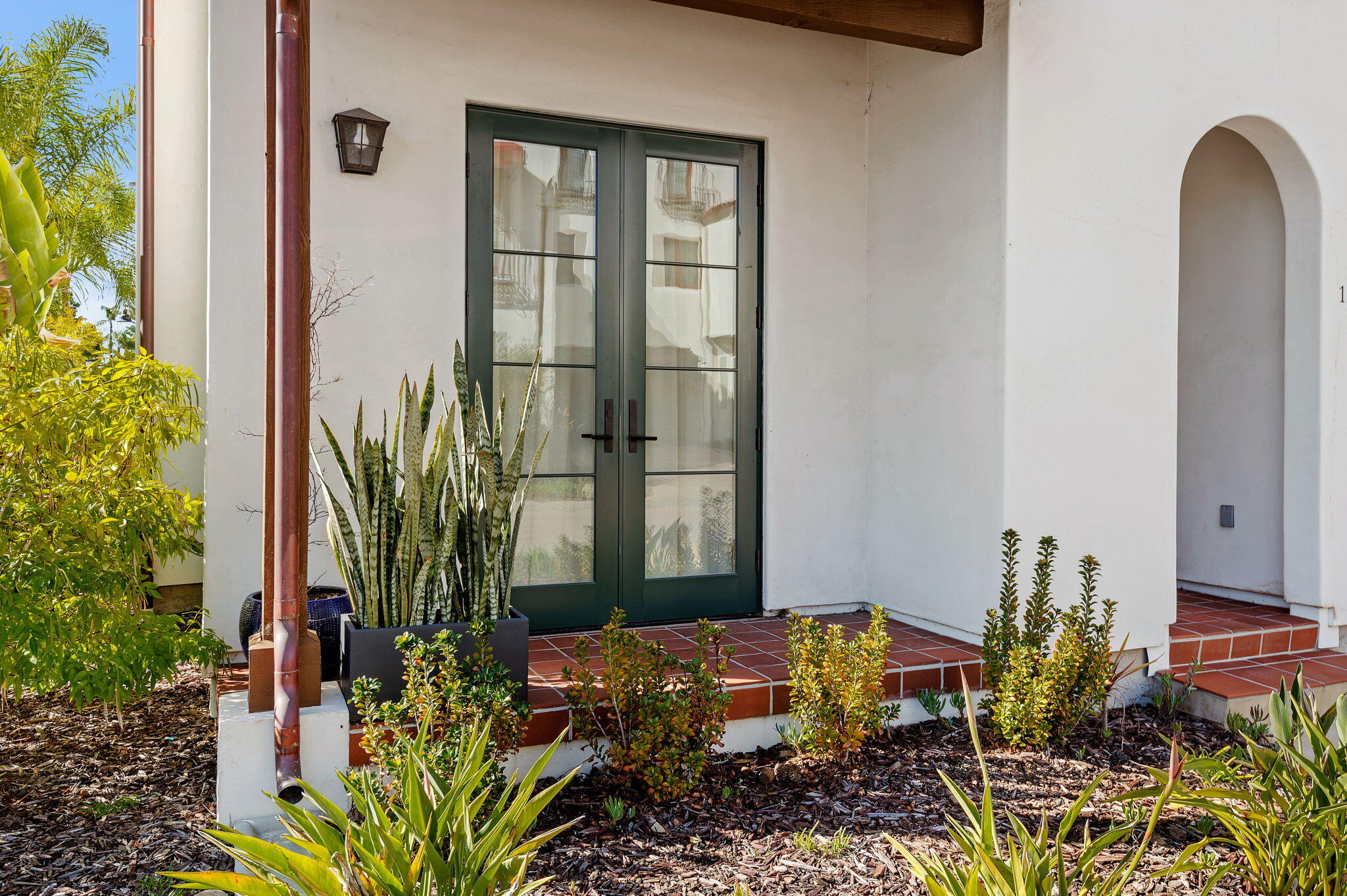 Front entrance with dark green glass double doors, red tile steps, and landscaped planting beds.