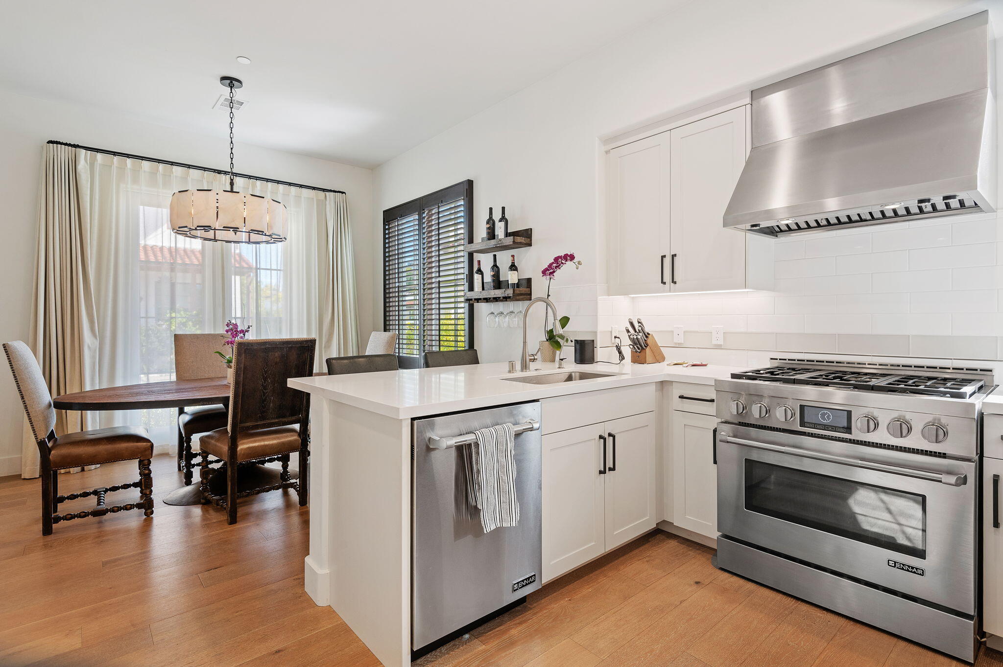 Bright white kitchen with a large island, stainless range and hood, opening to a dining area.