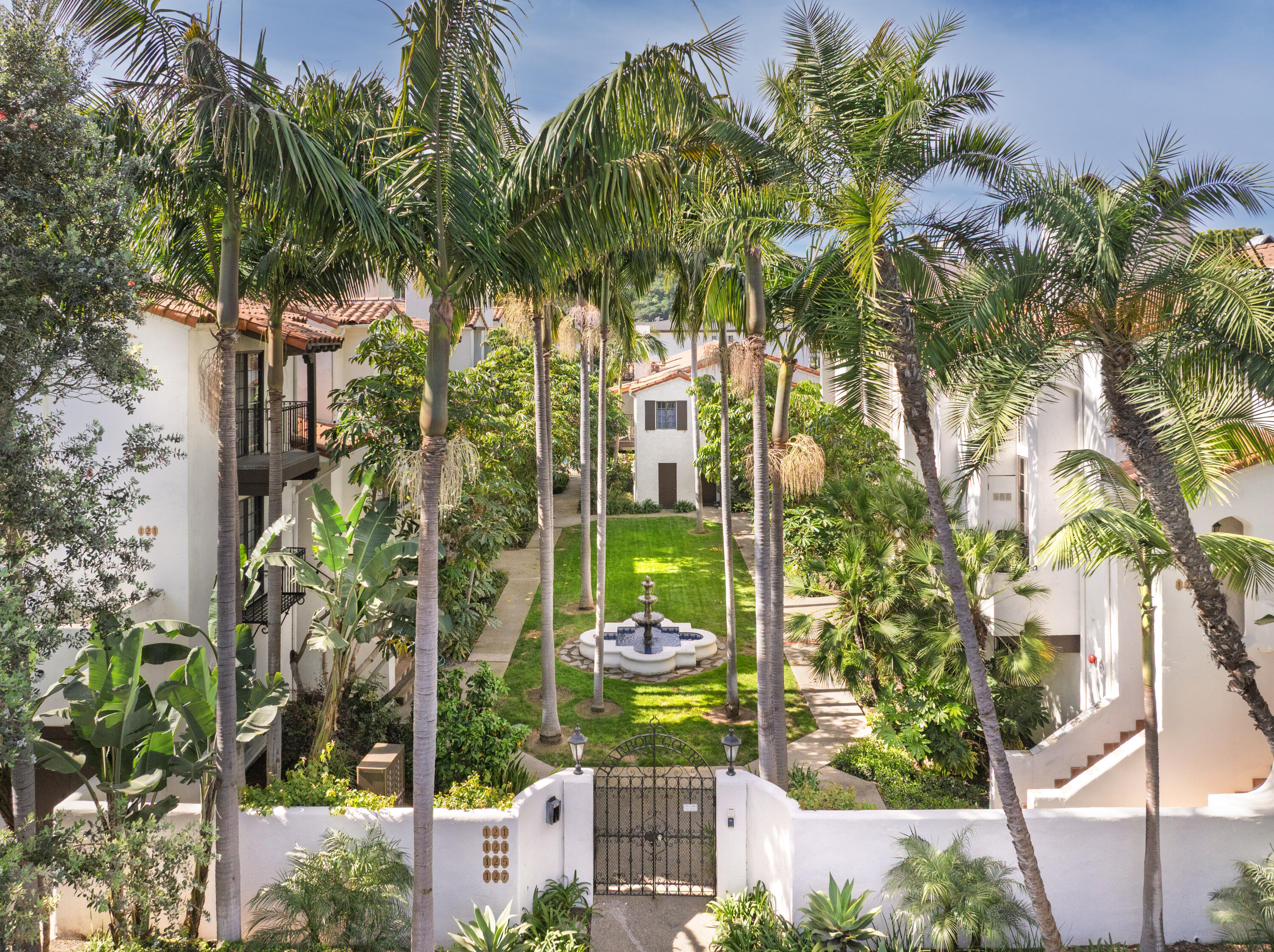Palm-lined residential courtyard with a central fountain and gated entrance.