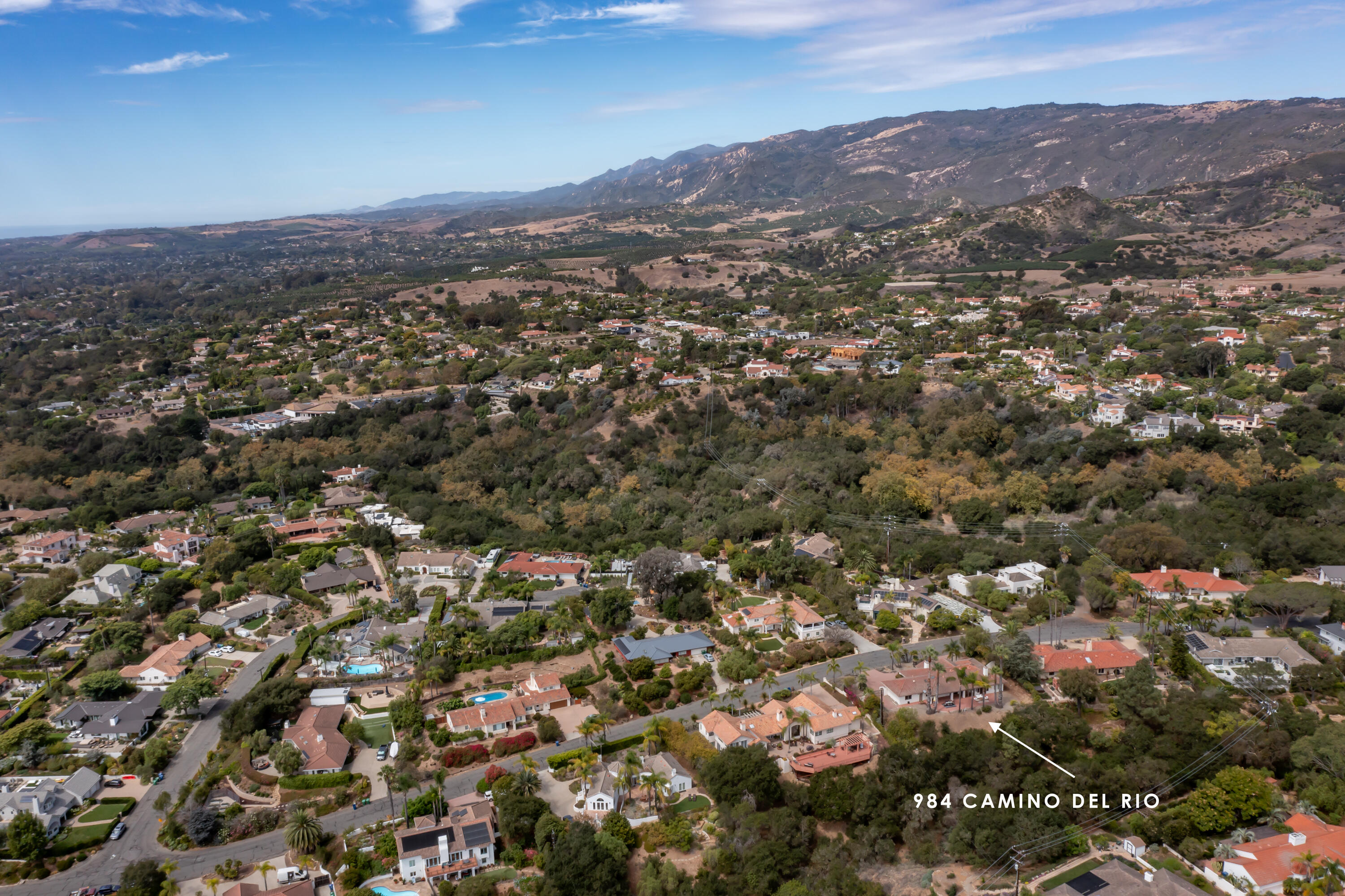 Aerial view of a home in a wooded neighborhood, marked by an arrow beneath distant hills.