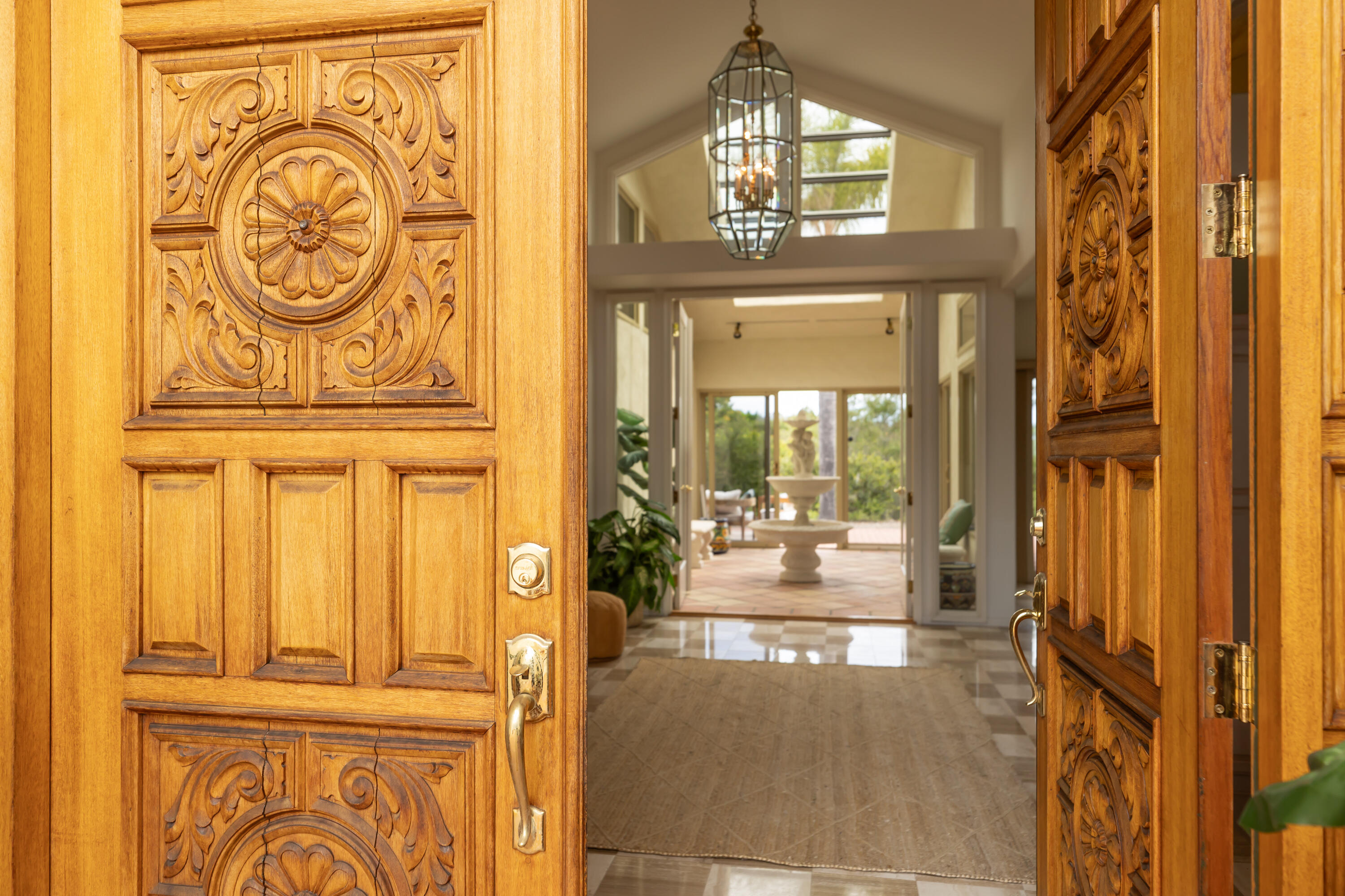 Open carved wooden doors frame a bright foyer and courtyard fountain.