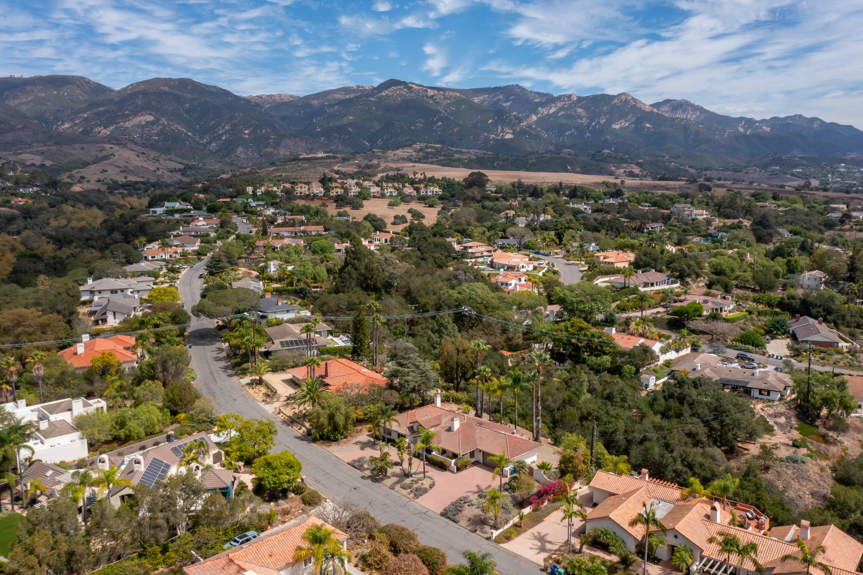 Aerial view of a residential neighborhood with terracotta-roofed homes and mountains beyond.