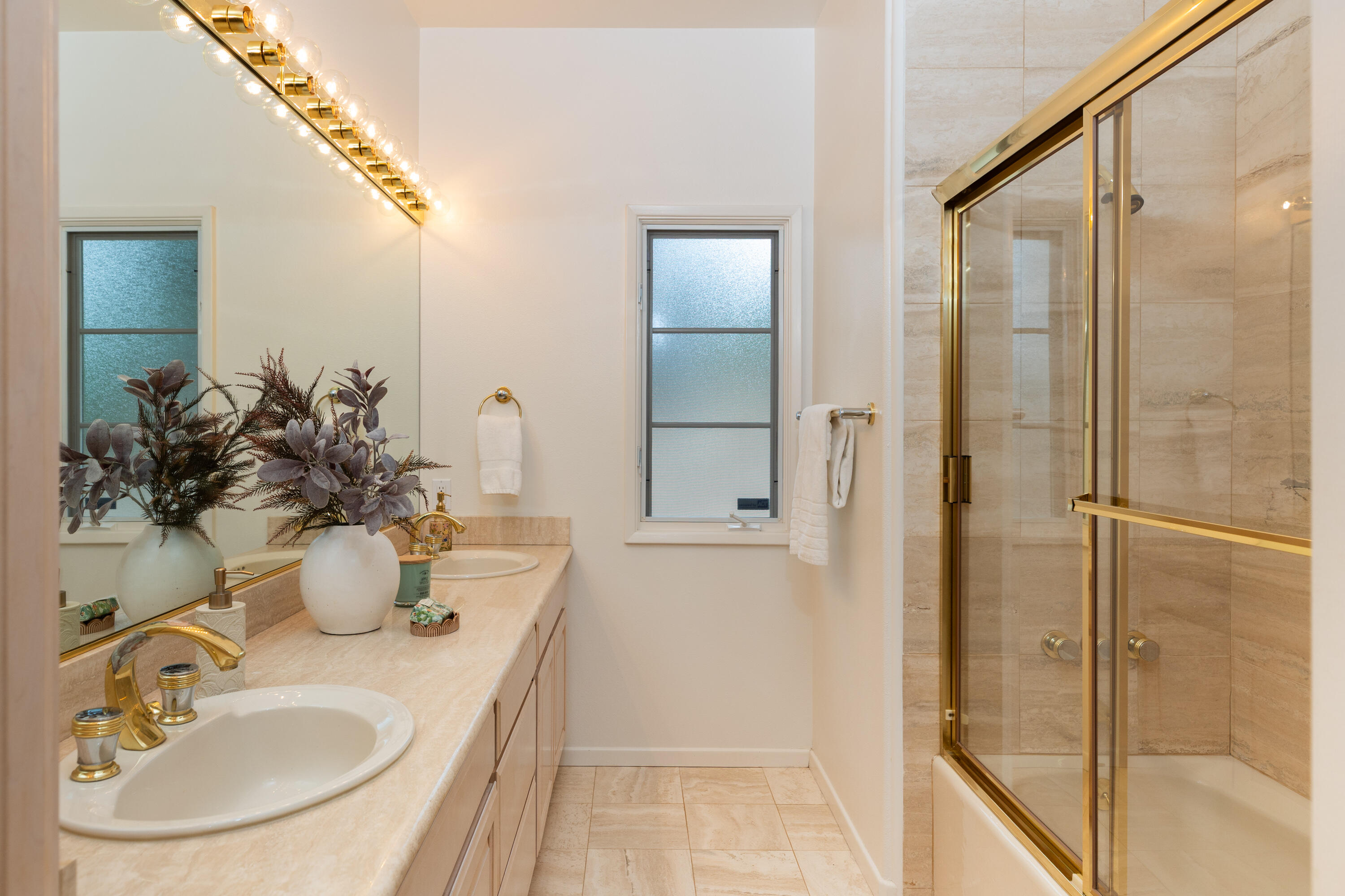 Bathroom with a pale stone vanity and glass shower enclosure framed in gold-toned metal.