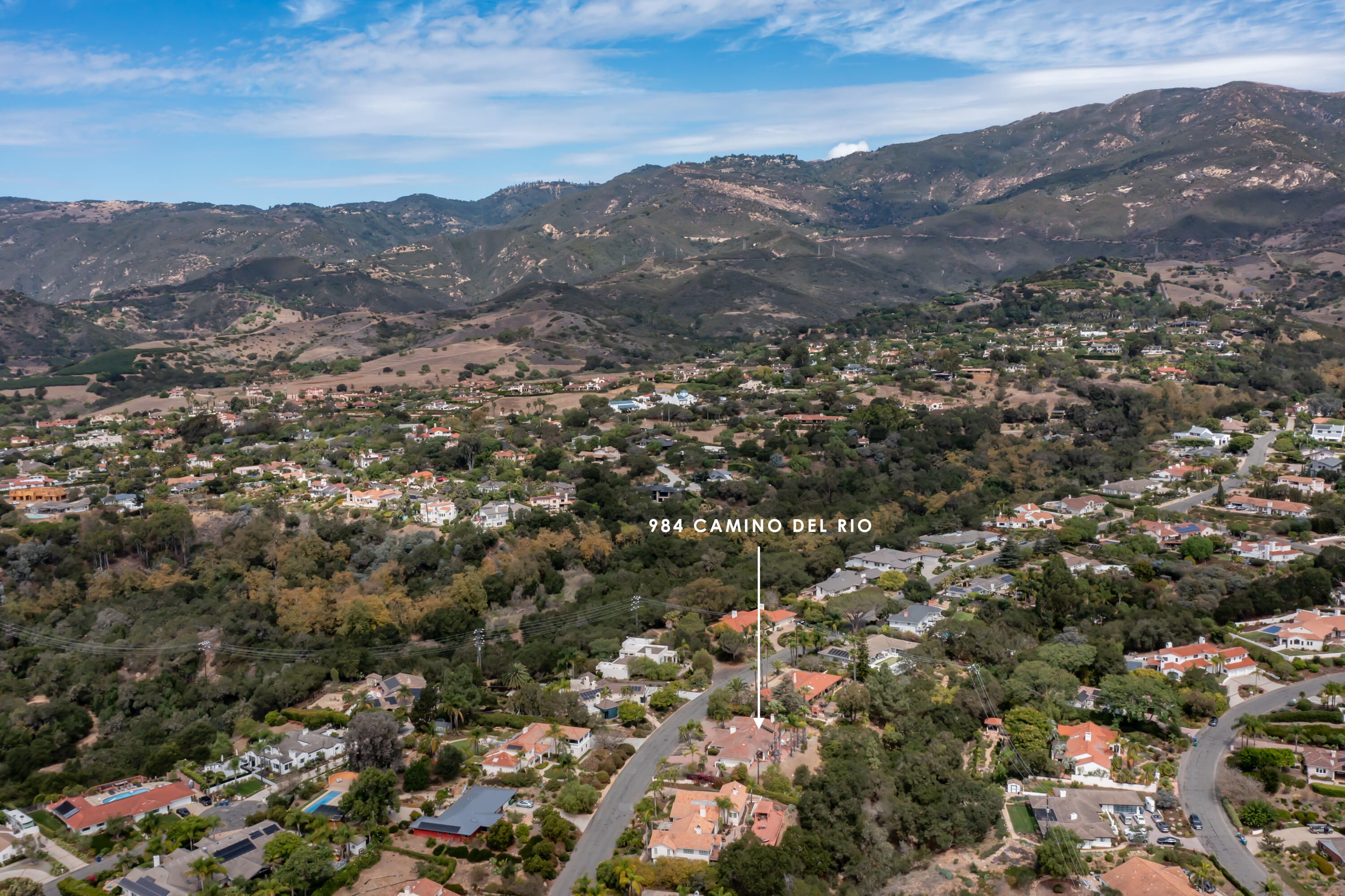 Aerial view of 984 Camino Del Rio, marked among tree-lined homes with mountains in the distance.