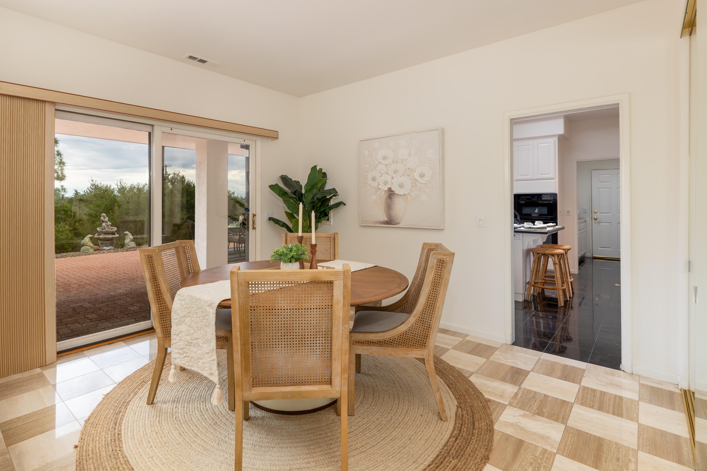 Dining room with a round wood table, woven chairs, and sliding doors overlooking a garden.