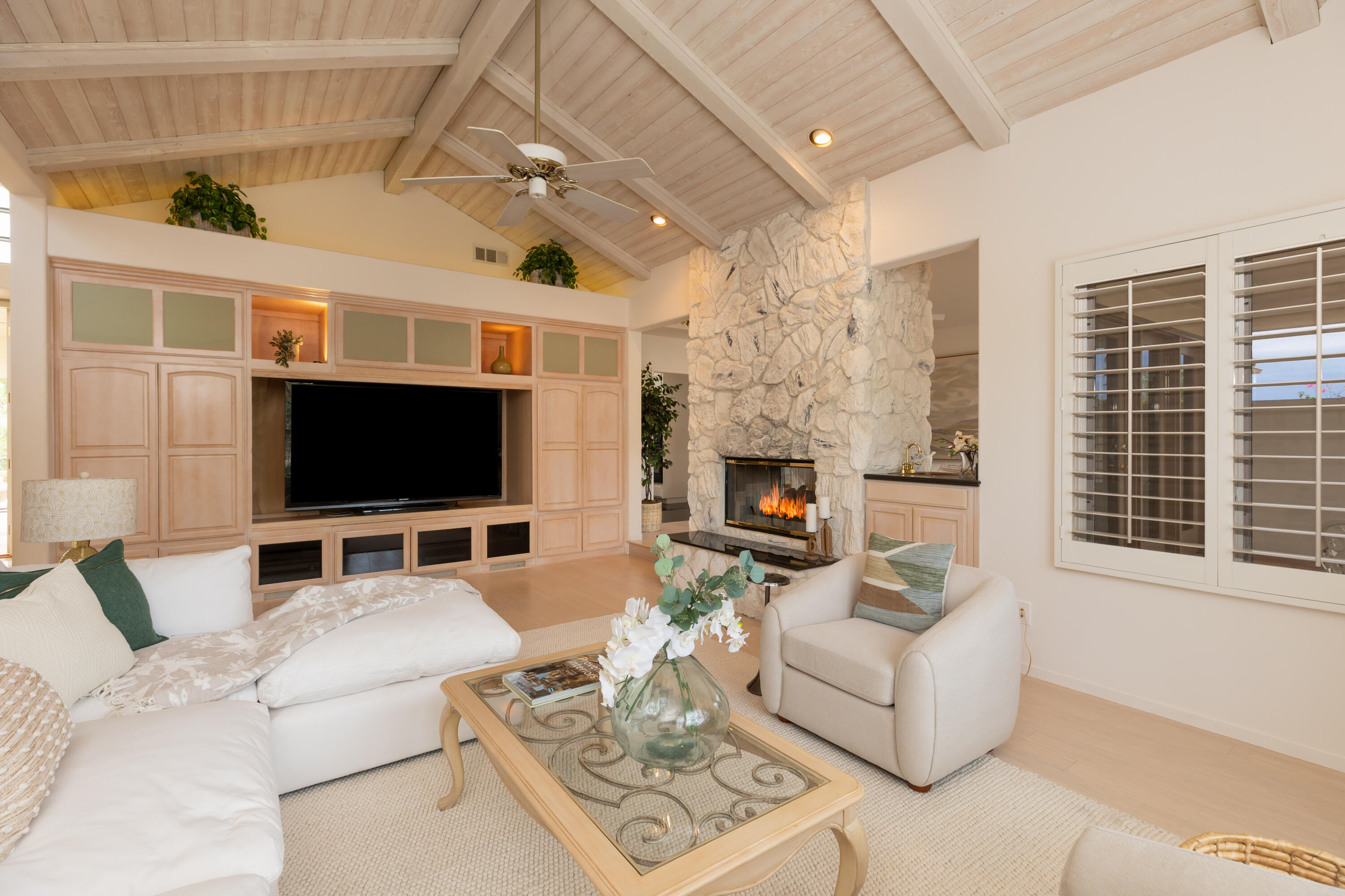 Living room with a vaulted wood ceiling, stone fireplace, and built-in television cabinetry.