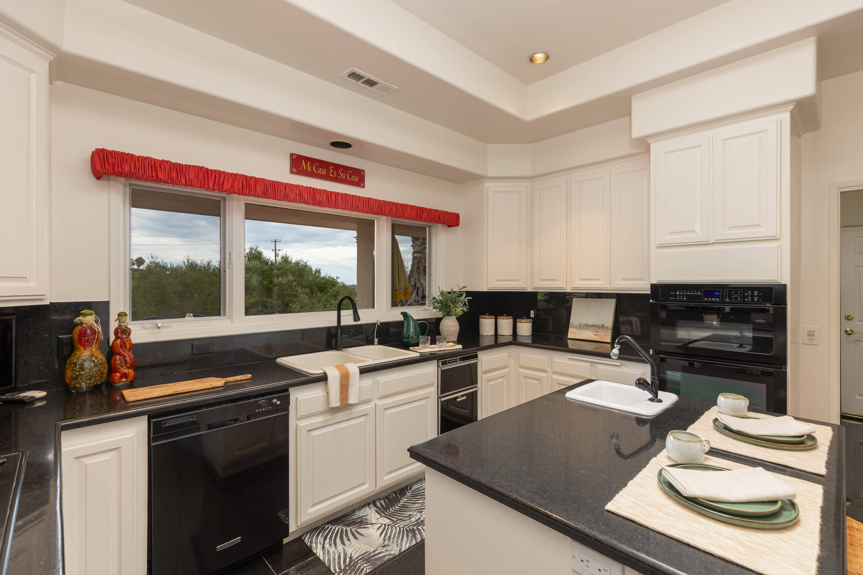 Kitchen with white paneled cabinets, black counters, a large island, and stacked double ovens.