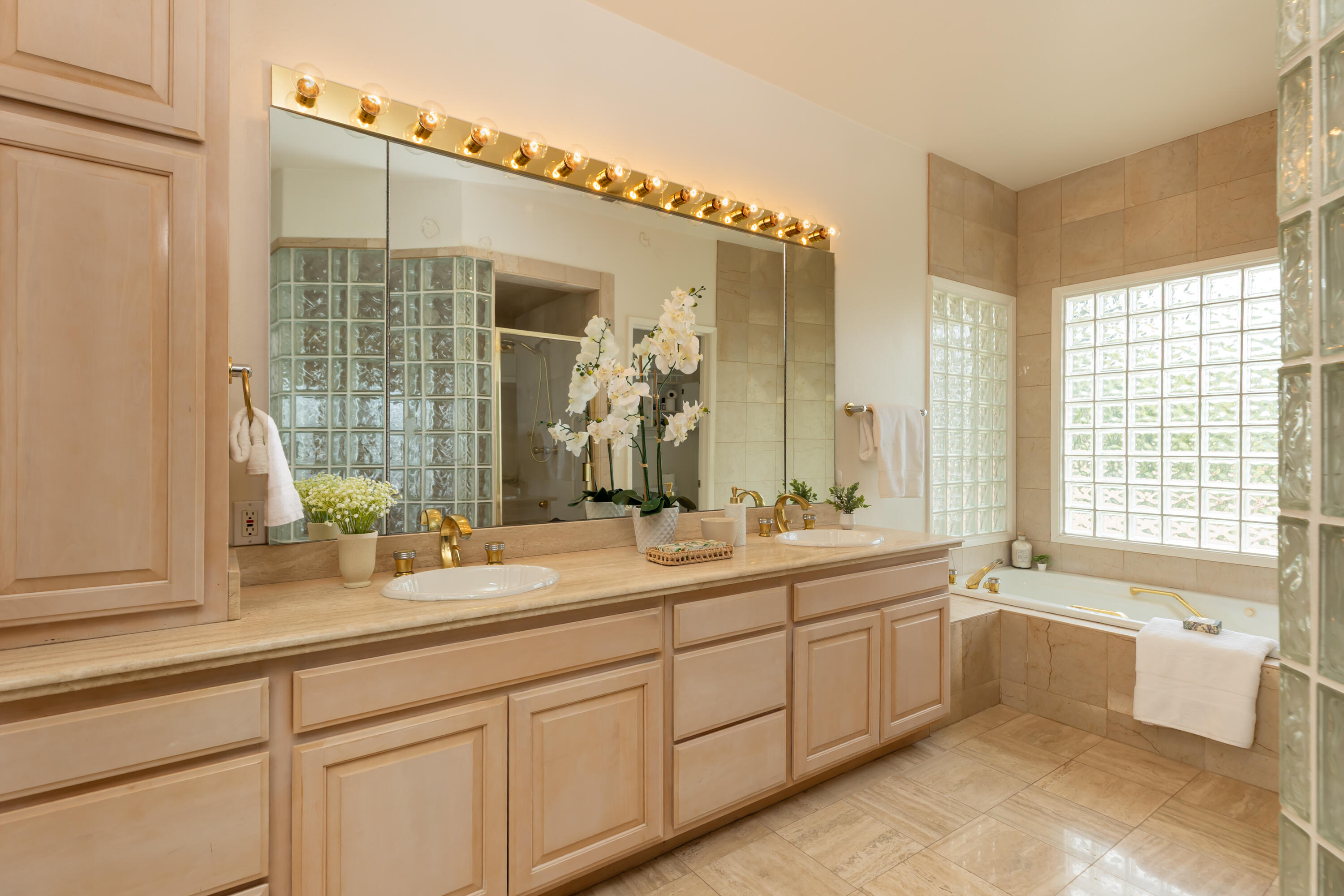 Bathroom with a double-sink vanity, glass-block windows, and a tiled soaking tub.