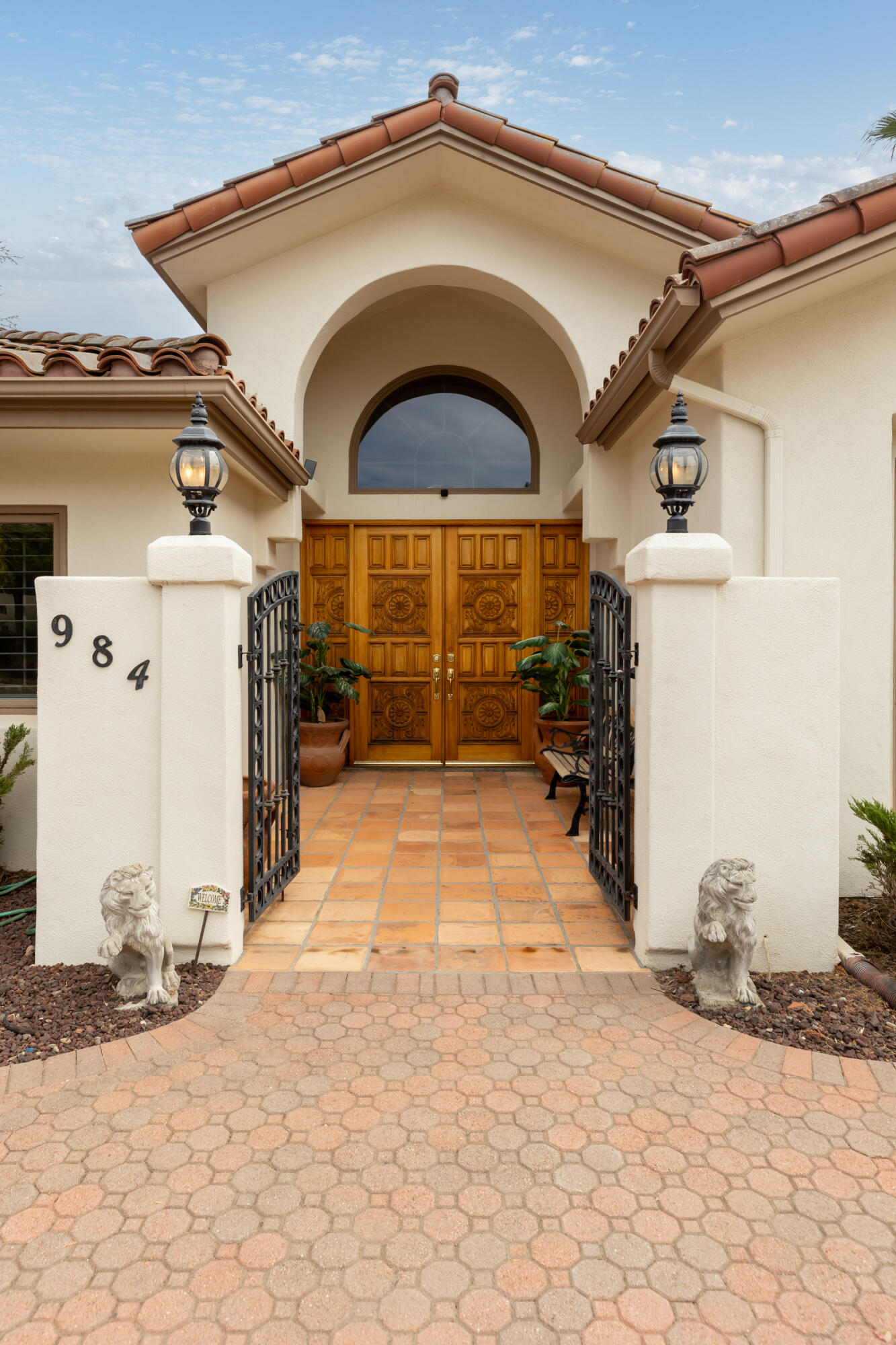 Home entrance with ornate wooden double doors, arched entry, wrought-iron gates, and stone lion statues.