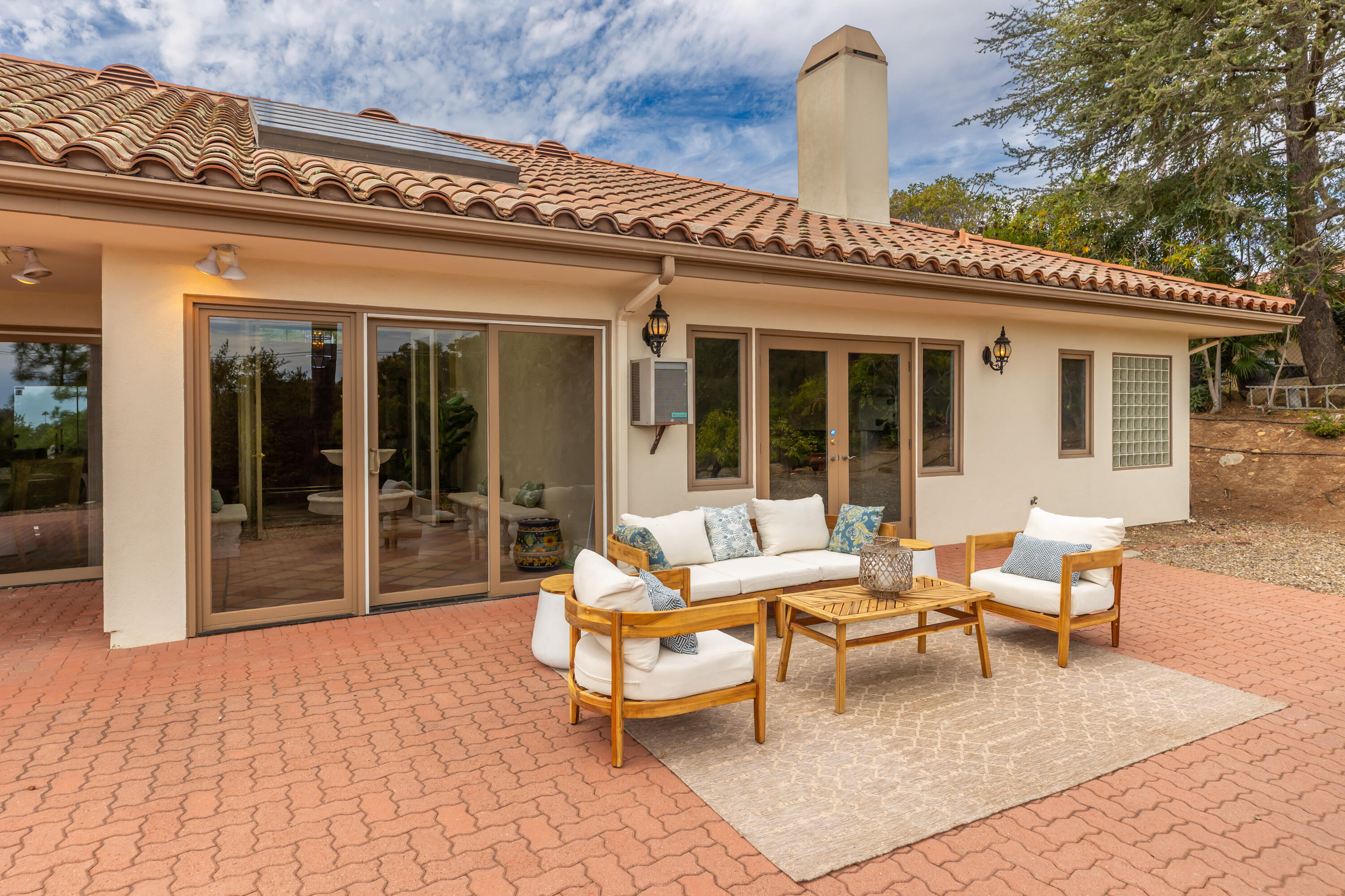 Rear patio with cushioned wooden seating, brick pavers, and large sliding glass doors.