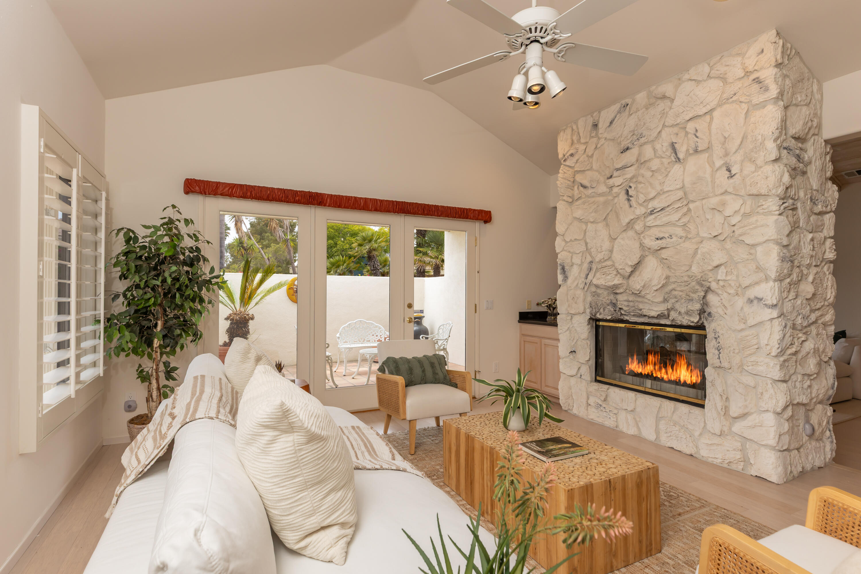 Living room with a dramatic white stone fireplace and glass doors opening to a palm-filled patio.