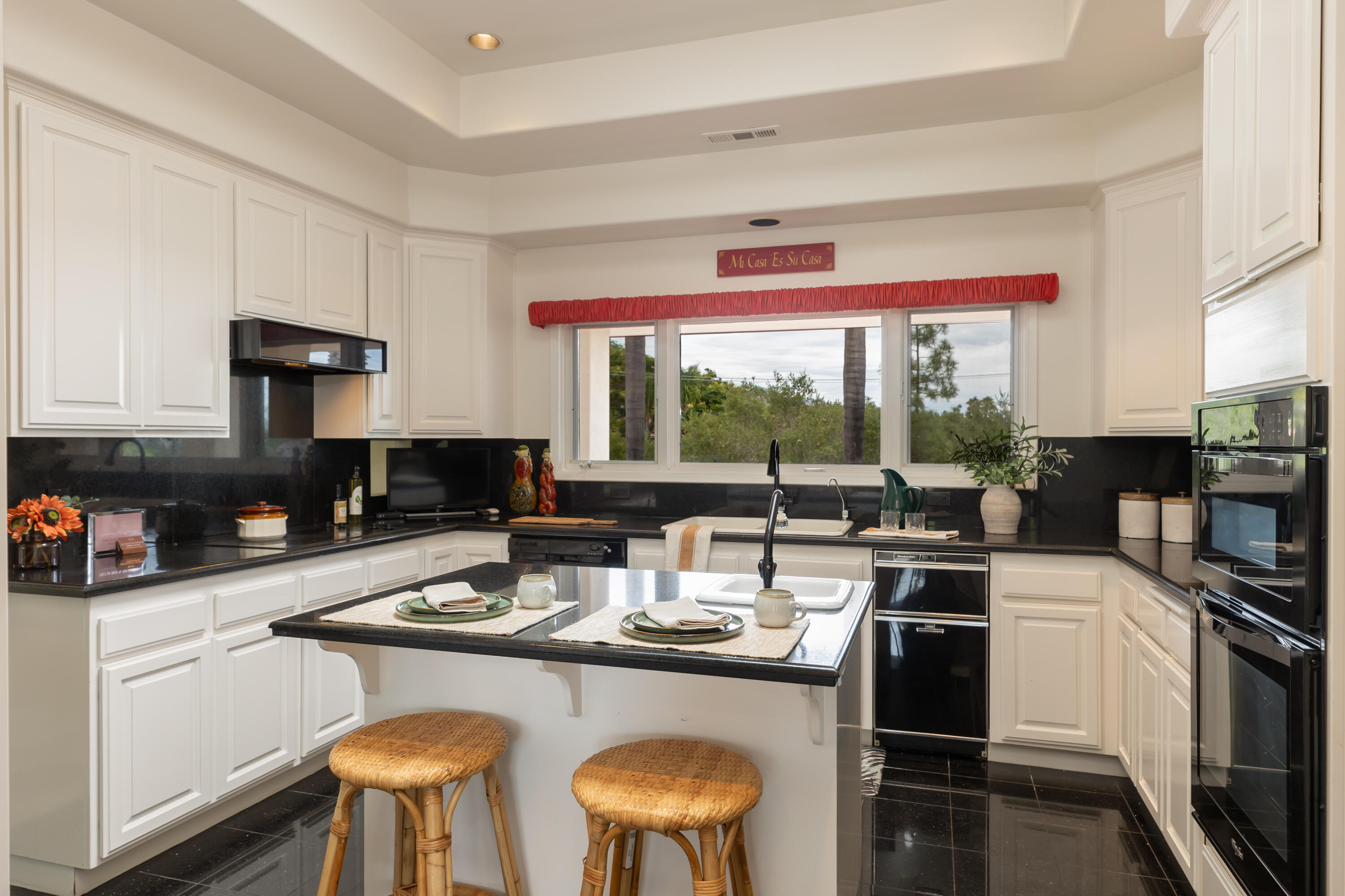 Kitchen with white cabinetry, black counters, a central island, and a wide window above the sink.