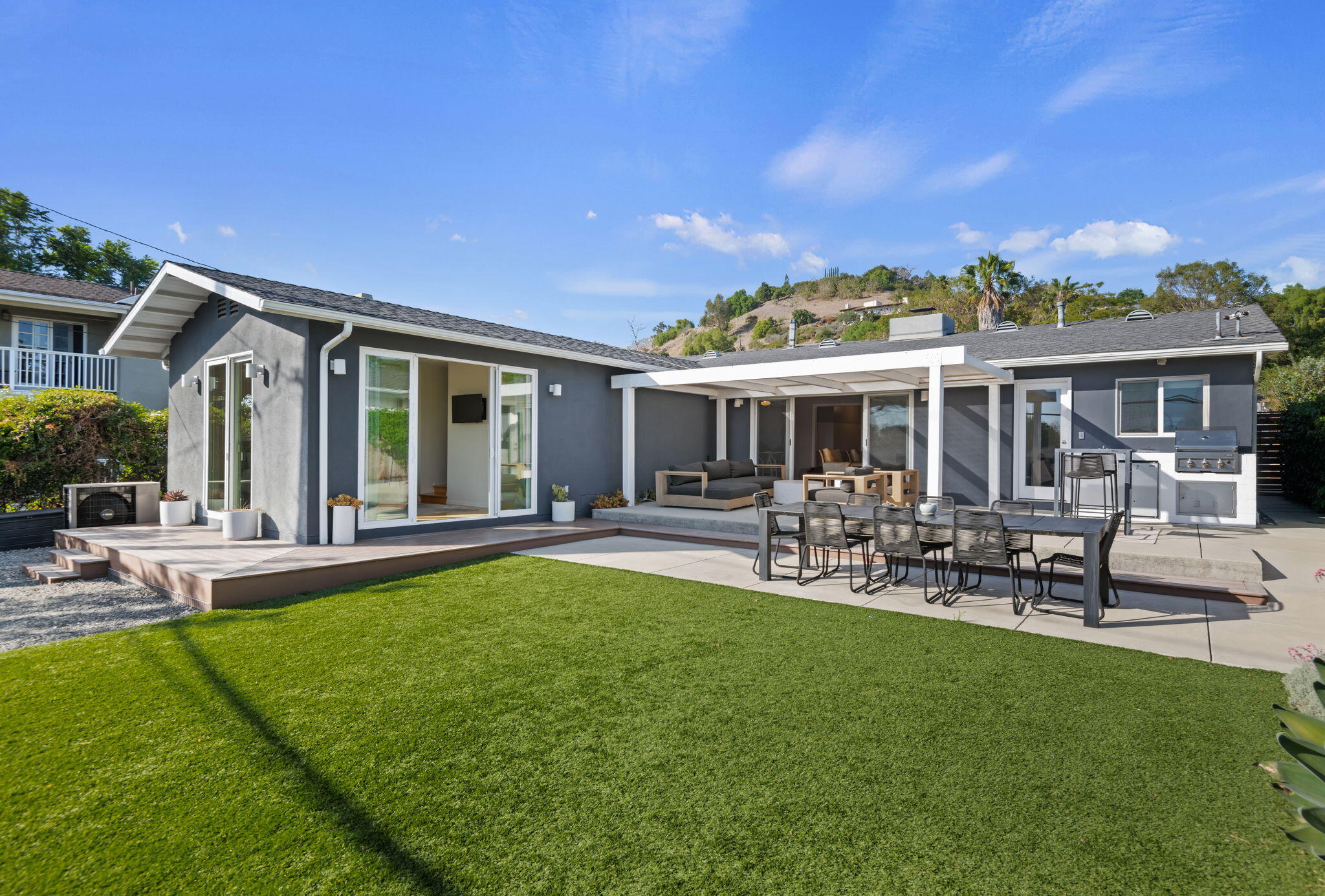 Modern gray home with a covered patio, outdoor dining area, grill, and broad green lawn.