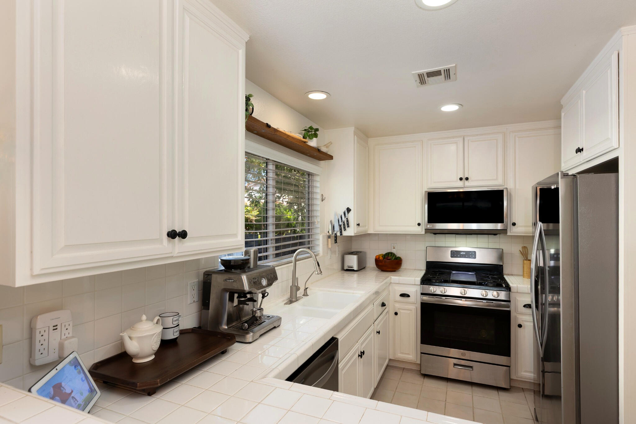 Kitchen with white cabinetry, tiled counters, stainless steel appliances, and a sink beneath a window.
