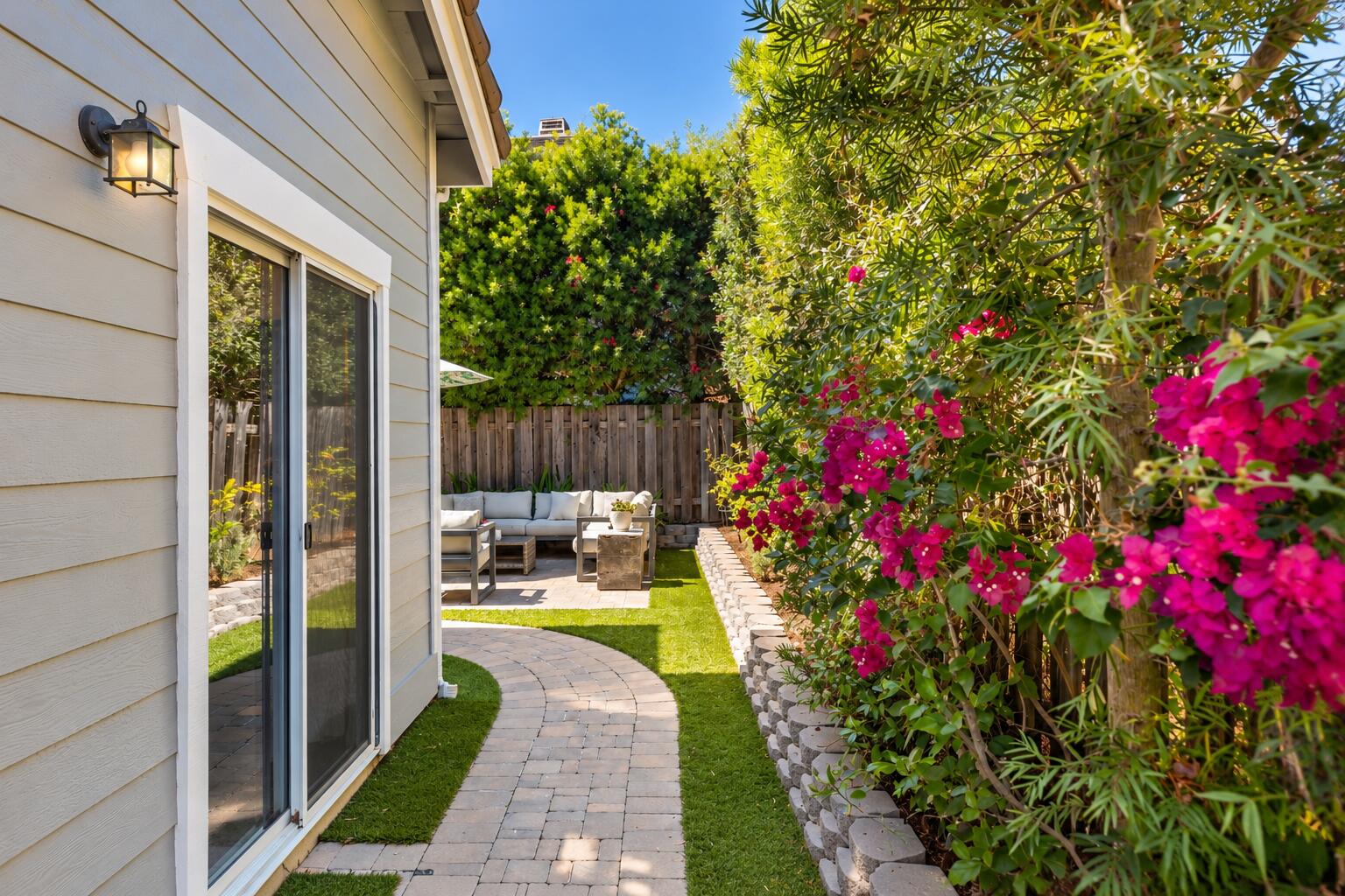 Backyard patio with curved paver walkway, outdoor seating, and bright pink bougainvillea.