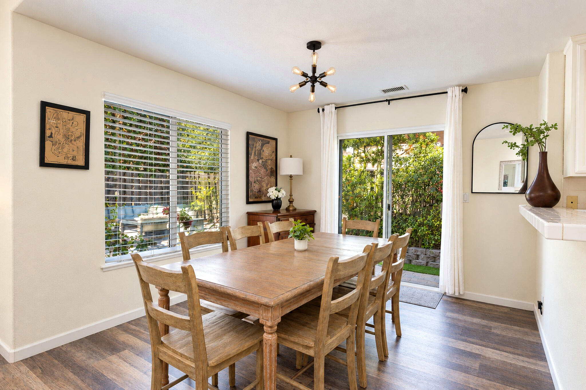 Dining room with a rustic wooden table, starburst chandelier, and sliding doors to a leafy patio.