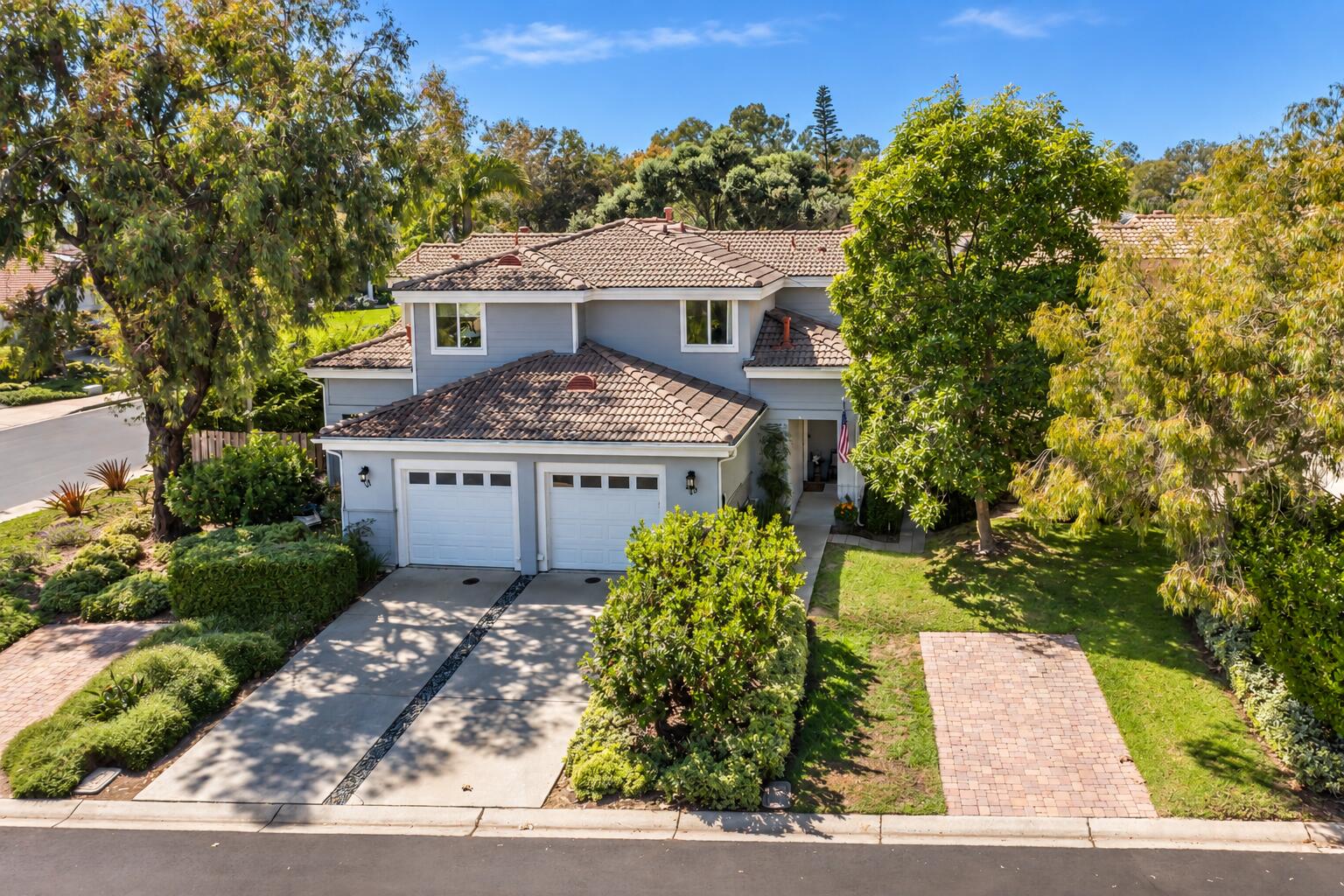 Aerial view of a gray two-story home with a tile roof, double garage, and mature landscaping.