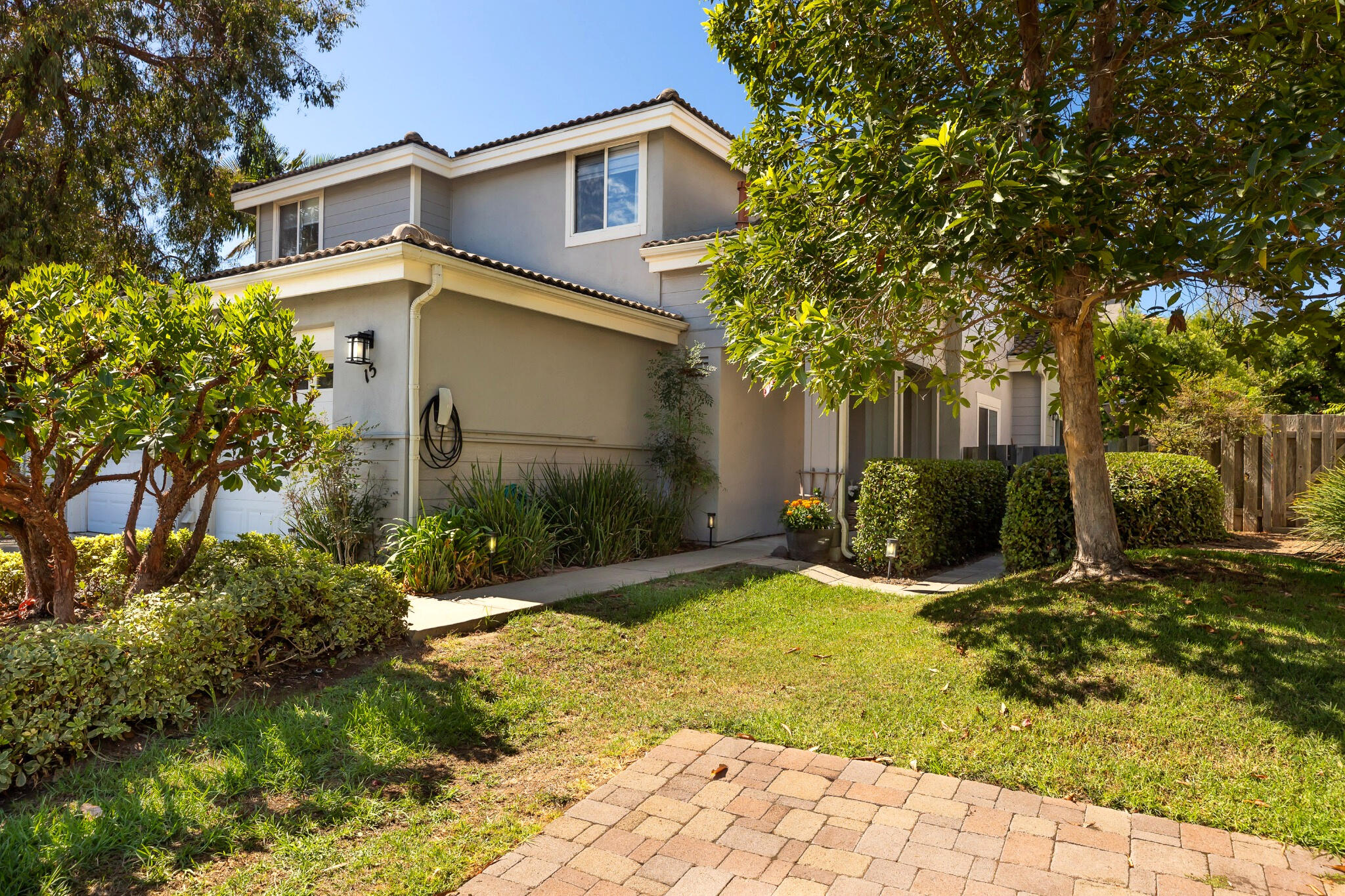 Two-story home exterior with gray siding, mature trees, and a landscaped lawn.