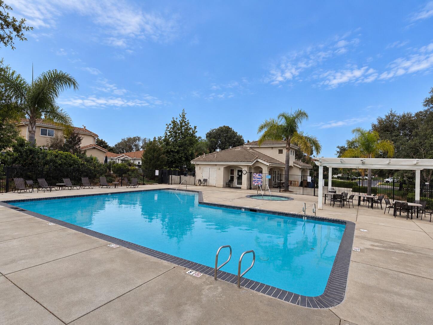 Community pool and spa with lounge chairs, a pool house, and covered patio dining area.