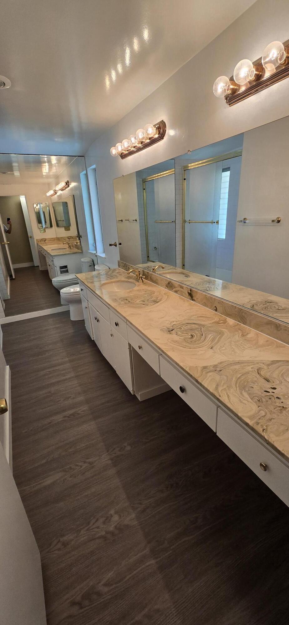 Long bathroom with double vanity, marble-pattern counters, mirrored walls, and glass-enclosed showers.