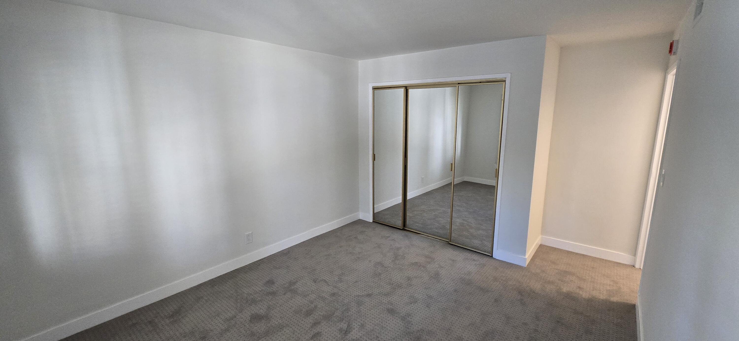 Empty bedroom with gray carpet and mirrored sliding closet doors.