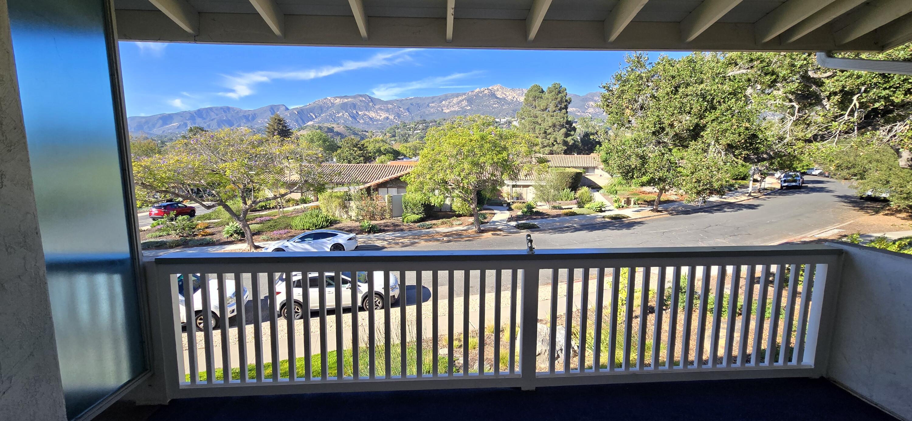 Covered balcony overlooking a tree-lined street and mountain range.