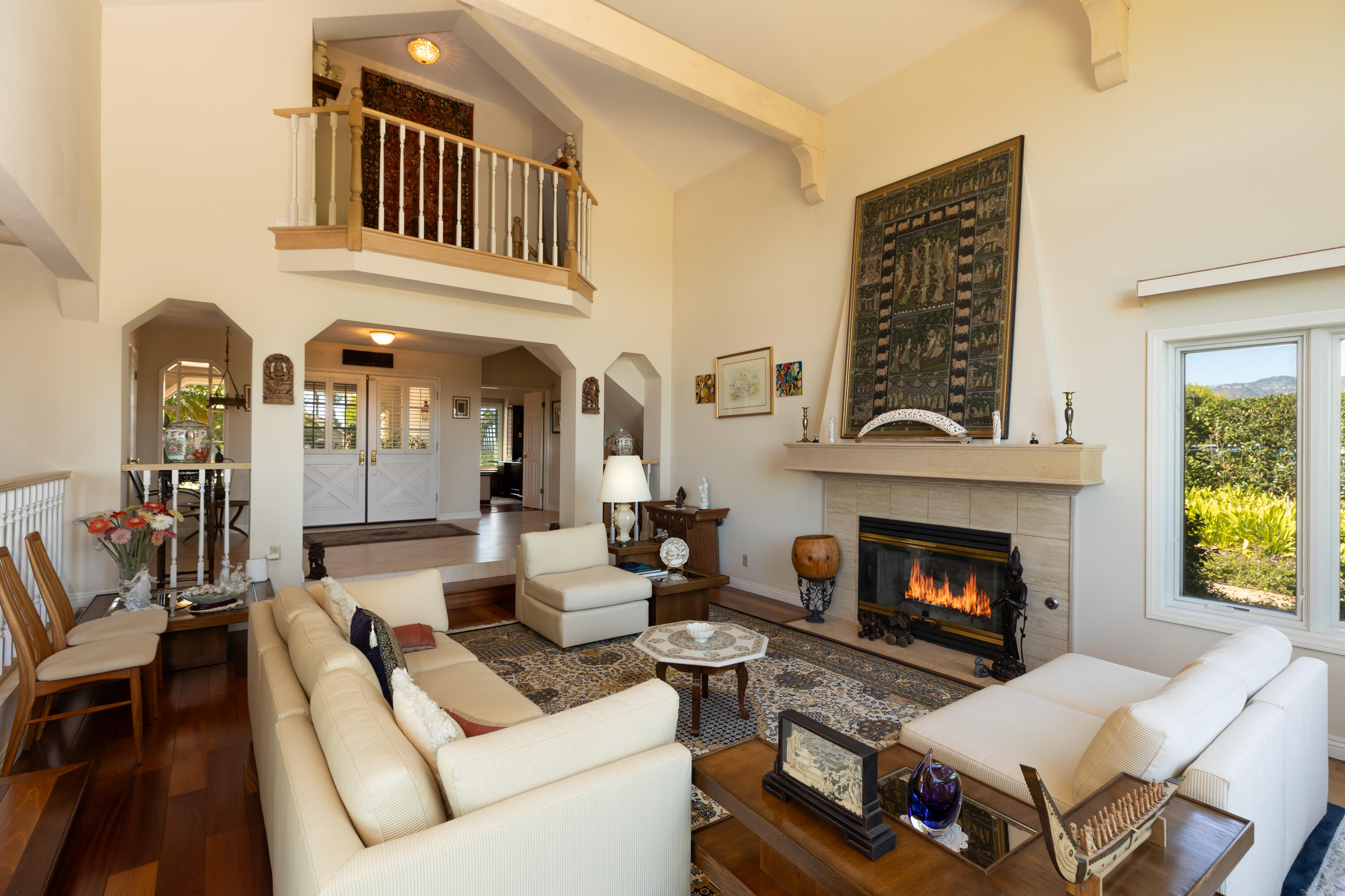 Living room with a vaulted ceiling, balcony, cream sofas, and a lit fireplace.