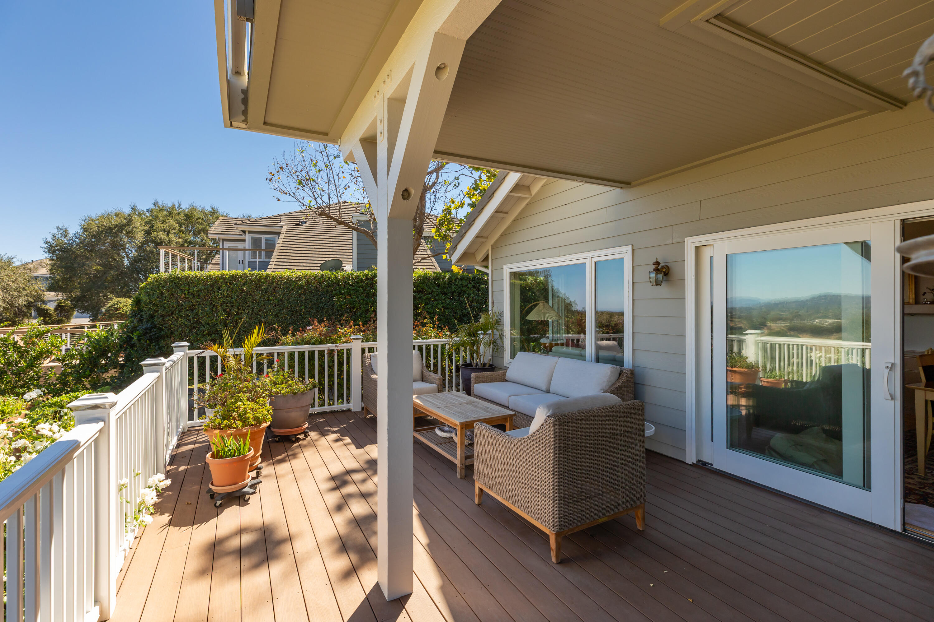 Covered deck with wicker seating, potted plants, white railing, and distant hills.