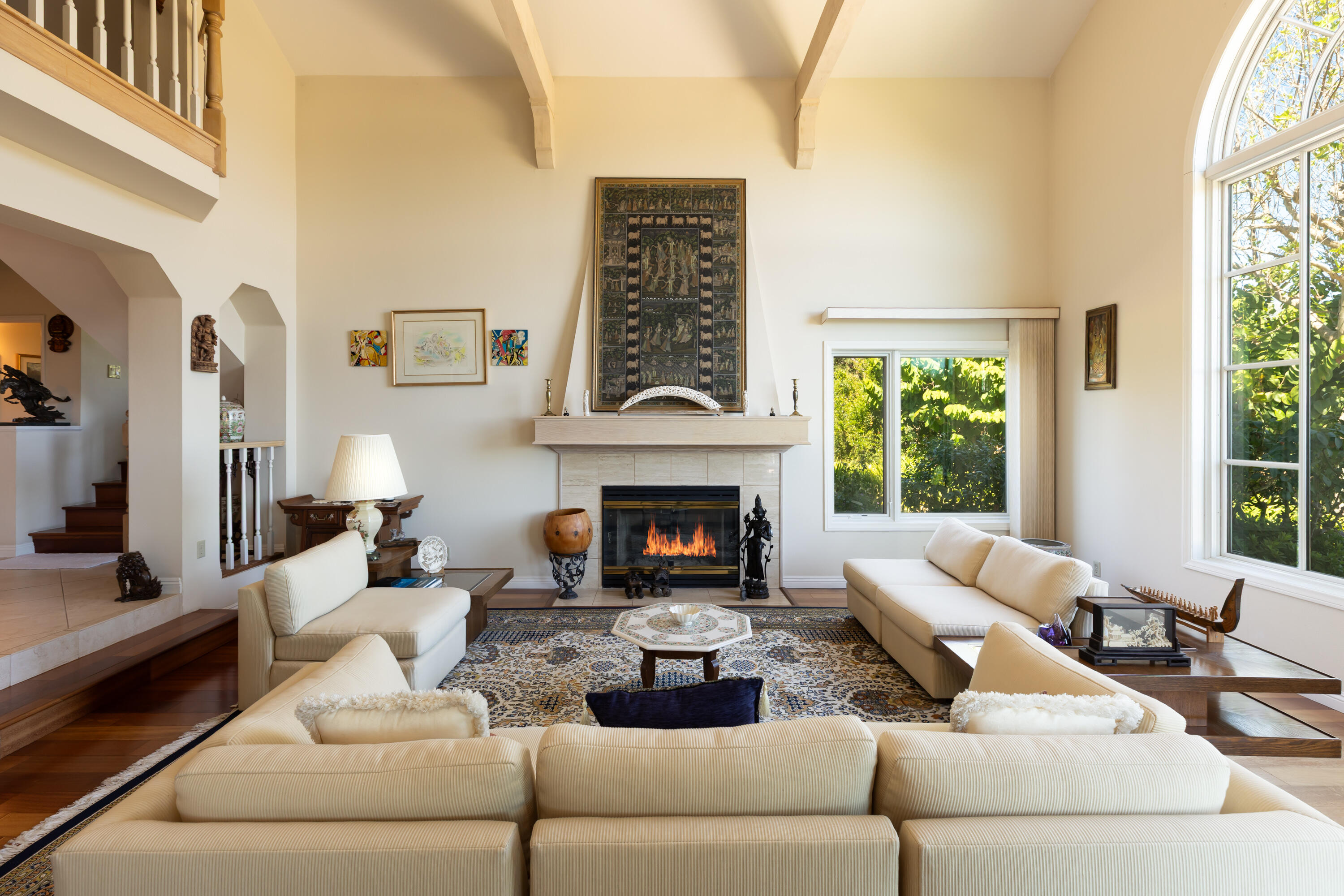 Living room with vaulted ceilings, a fireplace, cream sofas, and large windows overlooking greenery.