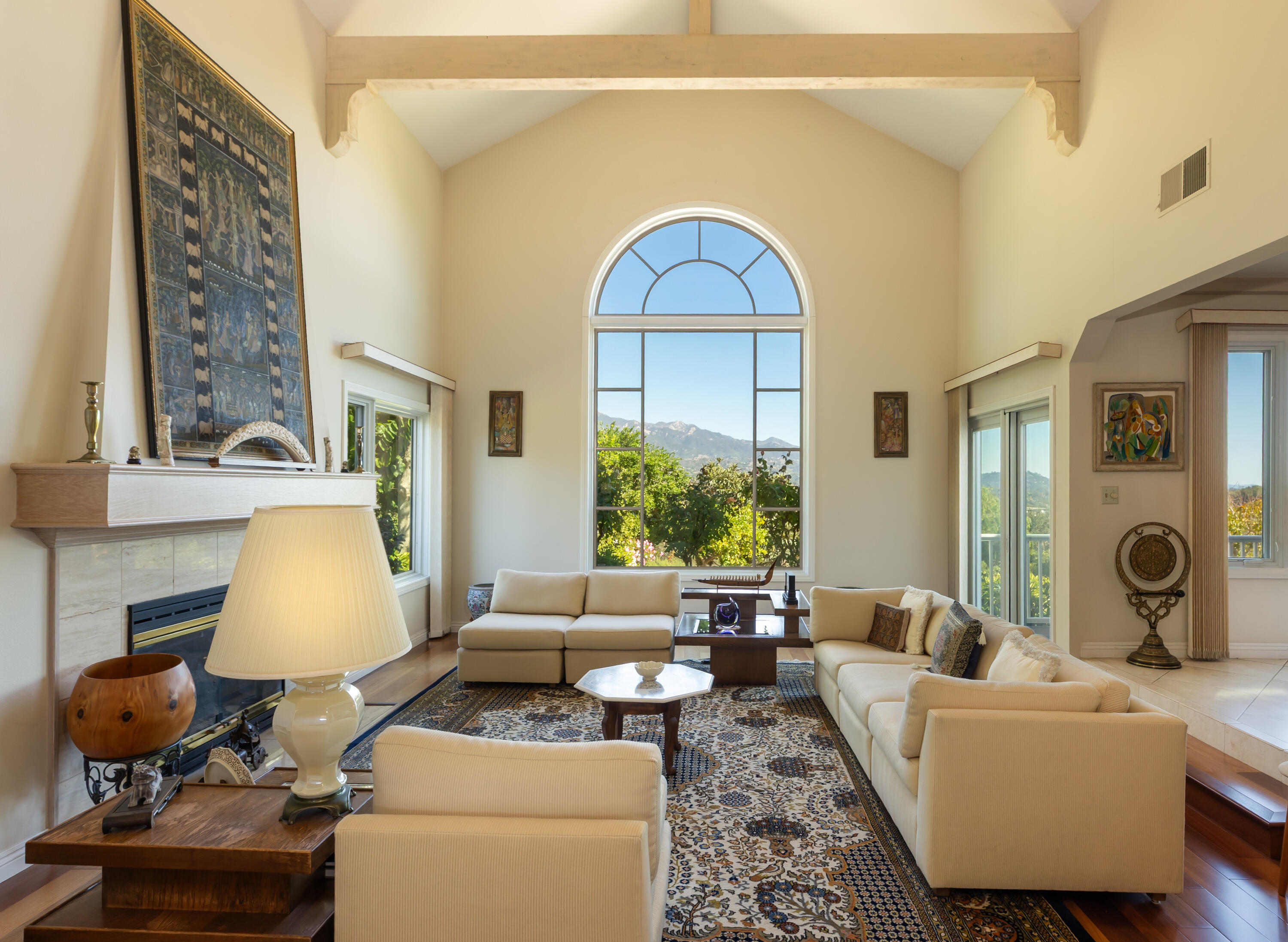 Living room with cream sofas, a fireplace, and a tall arched window framing mountain views.