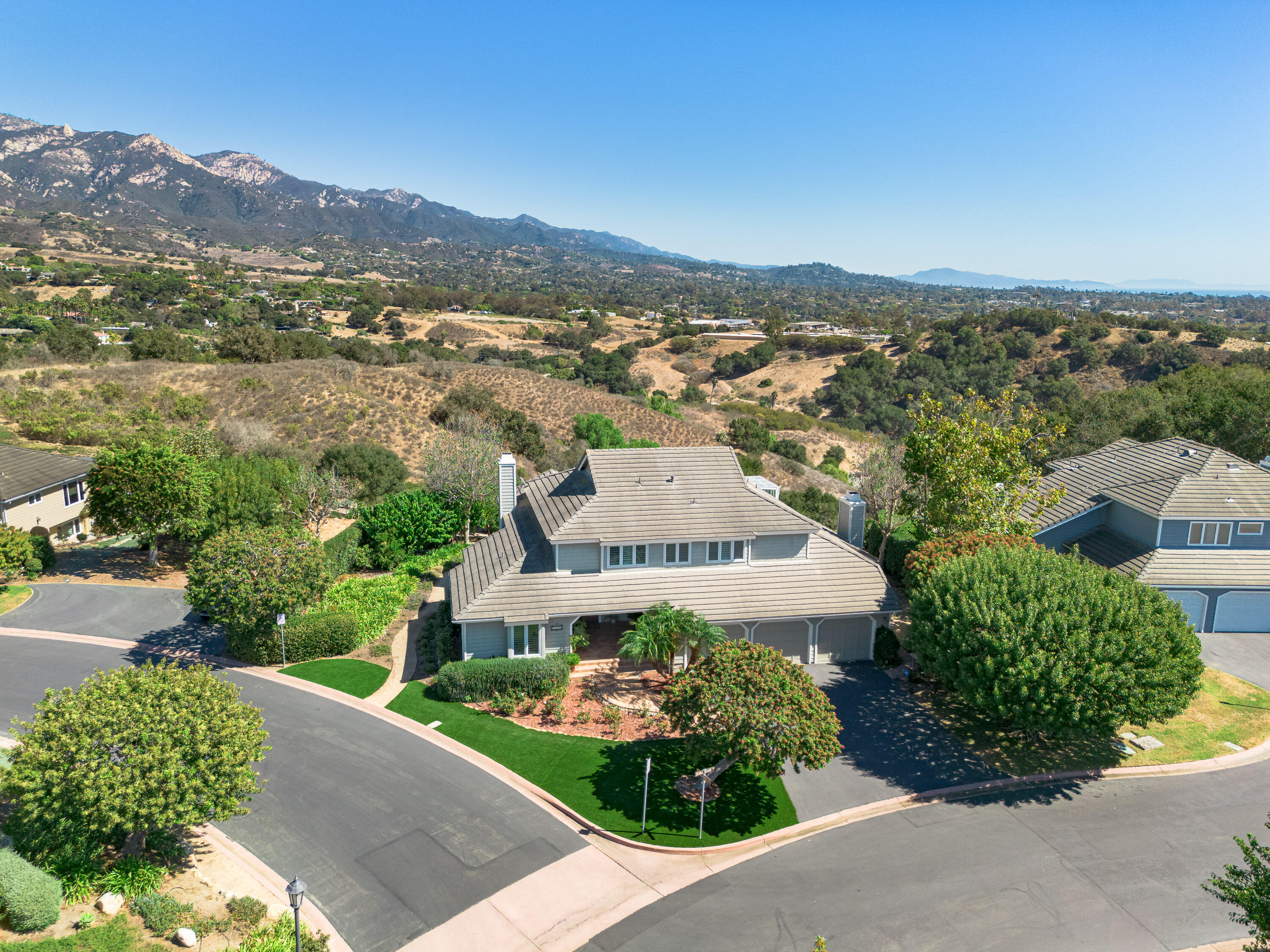 Aerial view of a corner home with landscaped grounds and mountains in the distance.