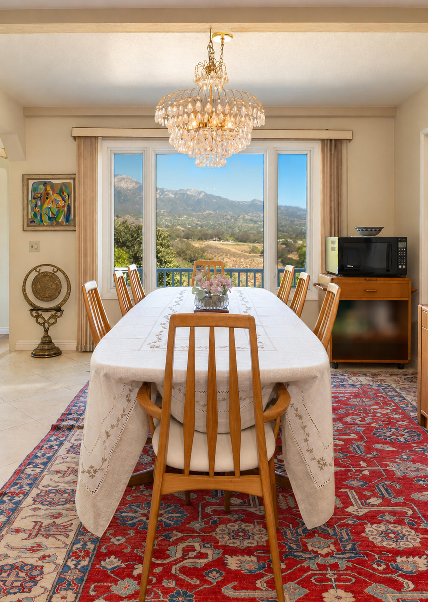 Dining room with a crystal chandelier, long table, and mountain views through large windows.