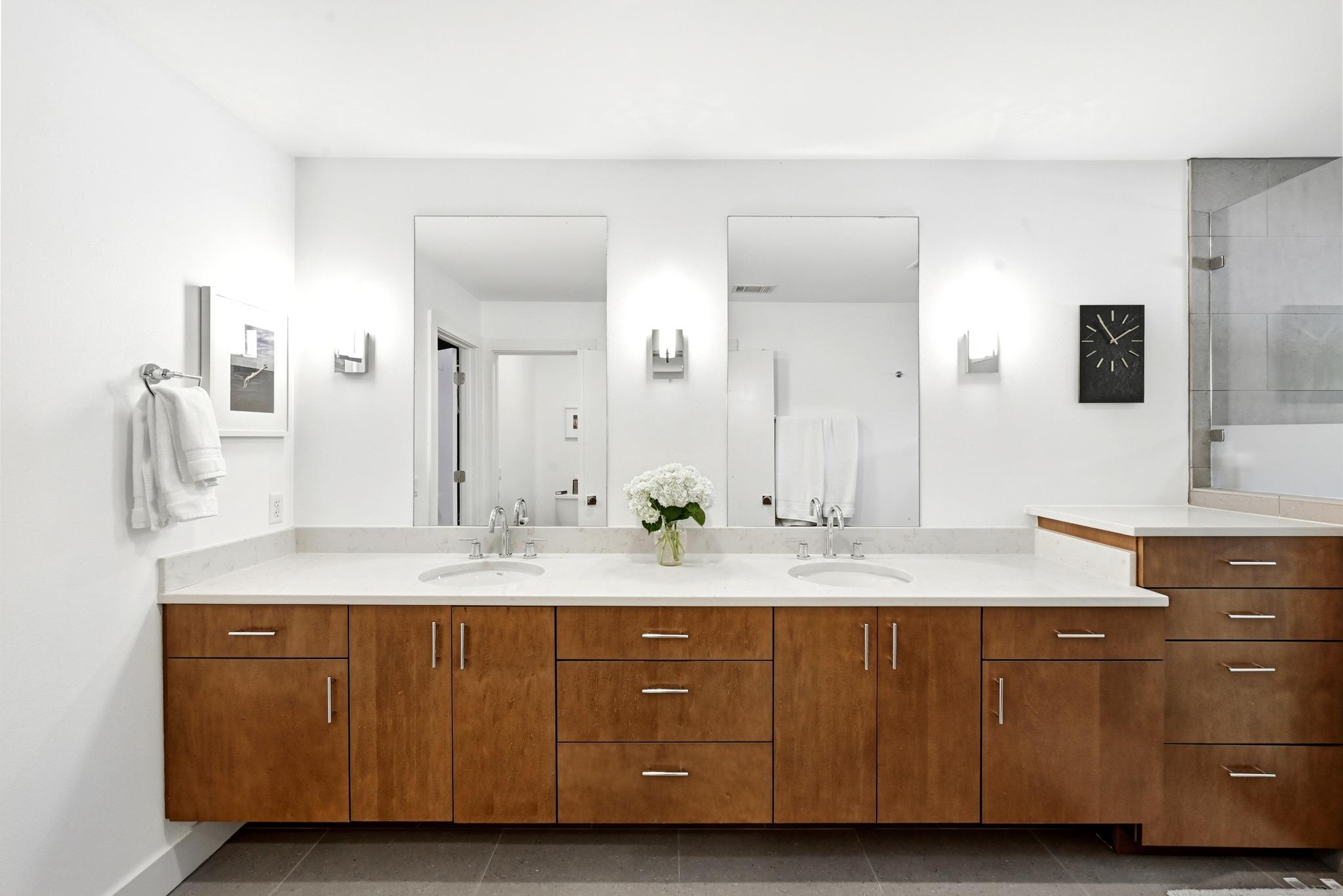 Modern bathroom with a double-sink vanity, warm wood cabinets, and a glass-enclosed shower.