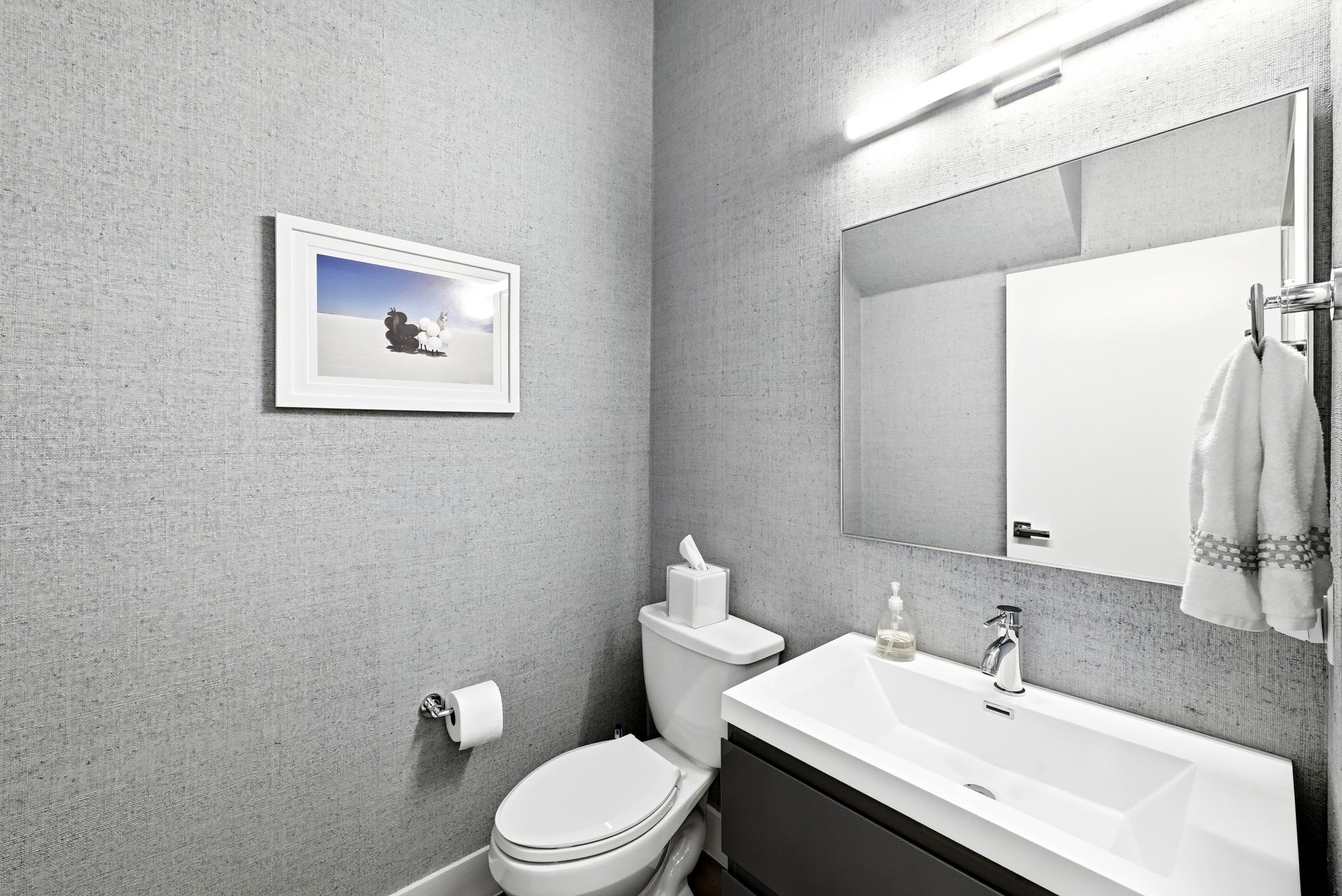 Modern bathroom with a white sink and toilet, large mirror, and gray textured walls.