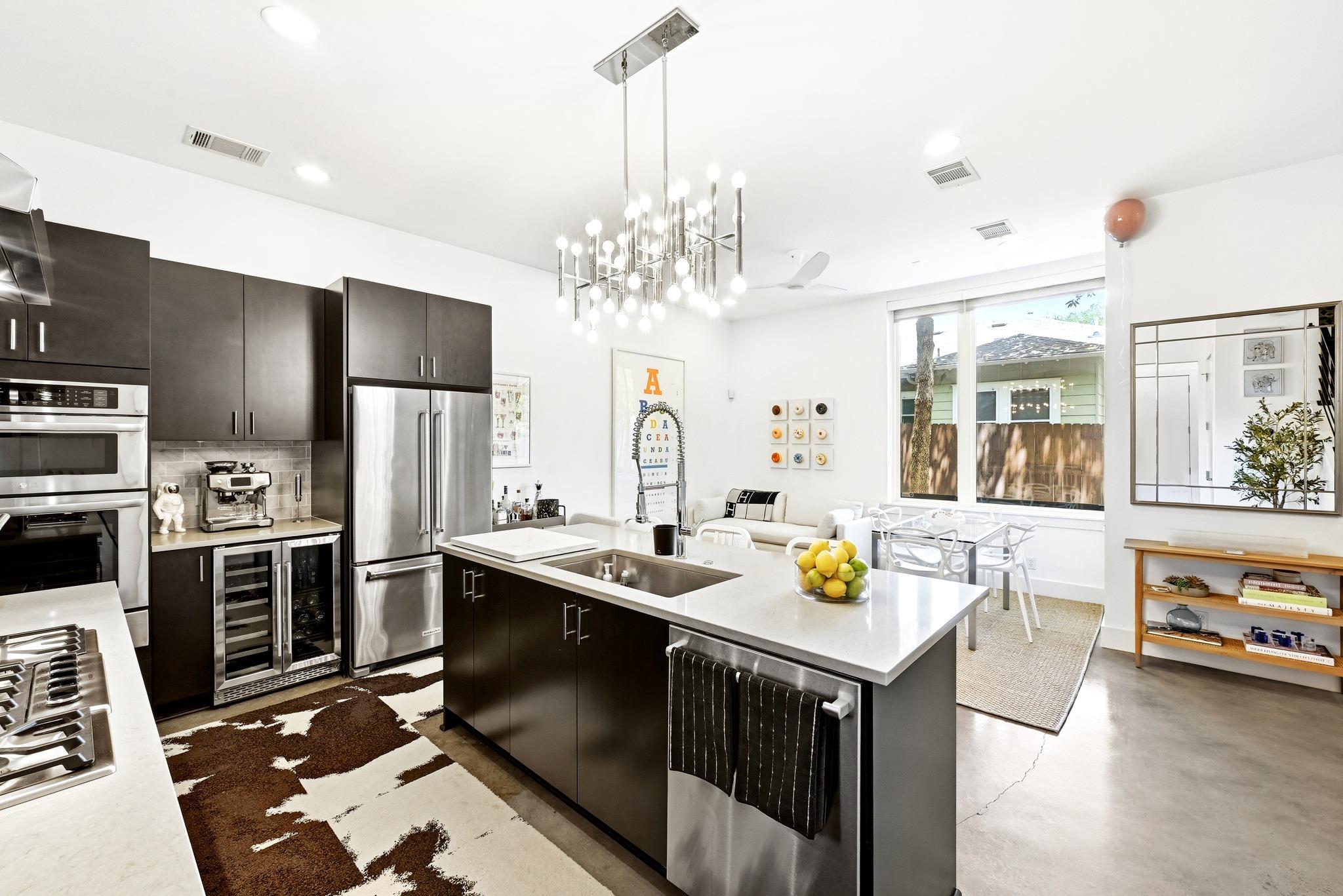 Modern kitchen with dark cabinets, stainless steel appliances, and a large island opening to a bright dining area.