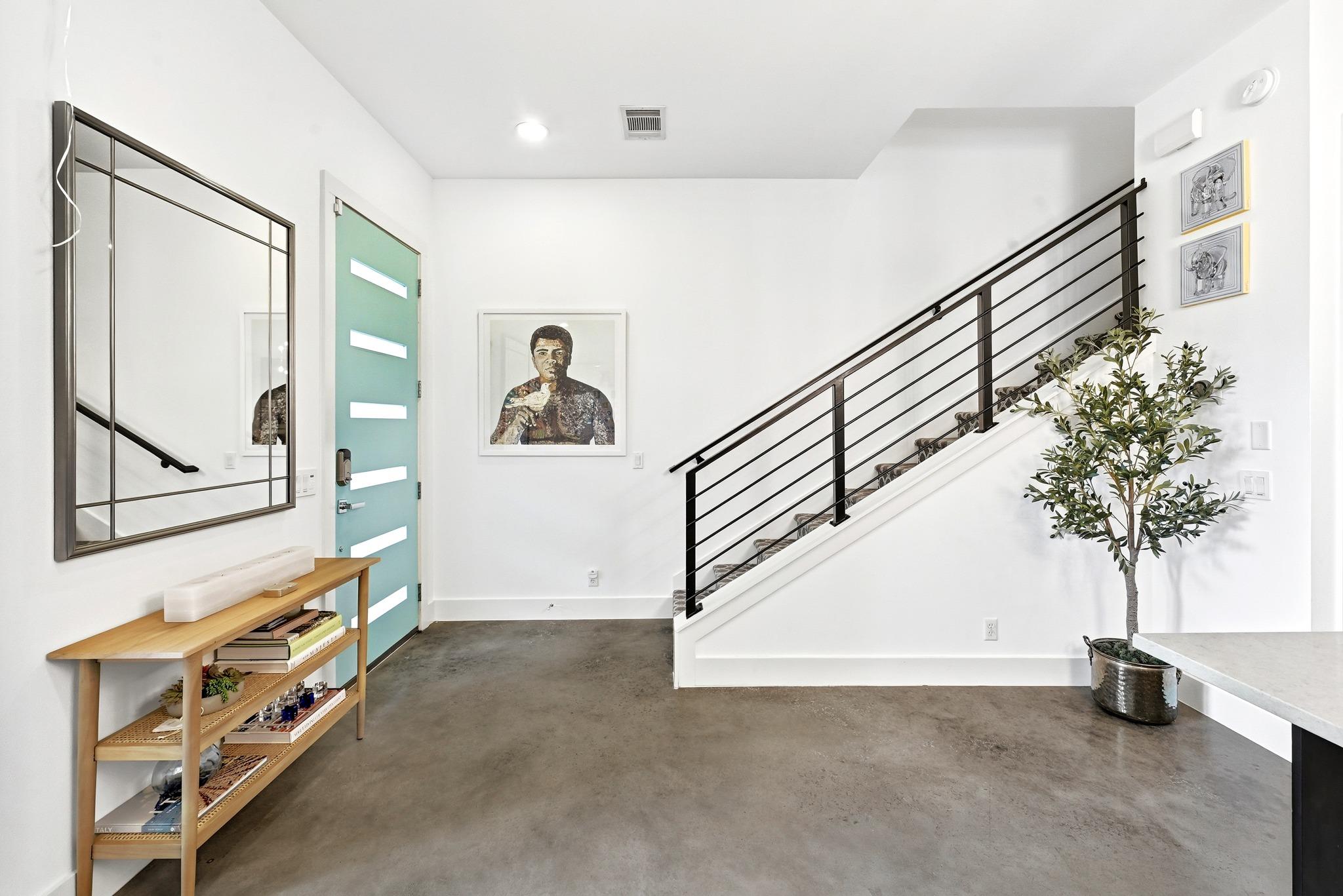 Modern entry foyer with a turquoise door, concrete floor, wood console, and black metal staircase.