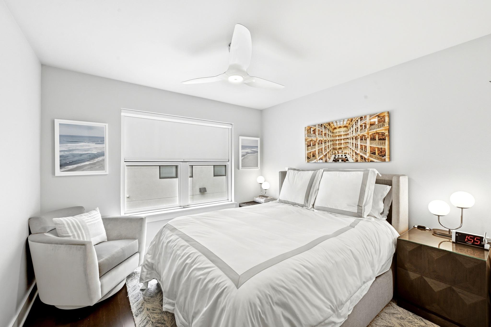 Furnished bedroom with a white bed, gray armchair, and ceiling fan.