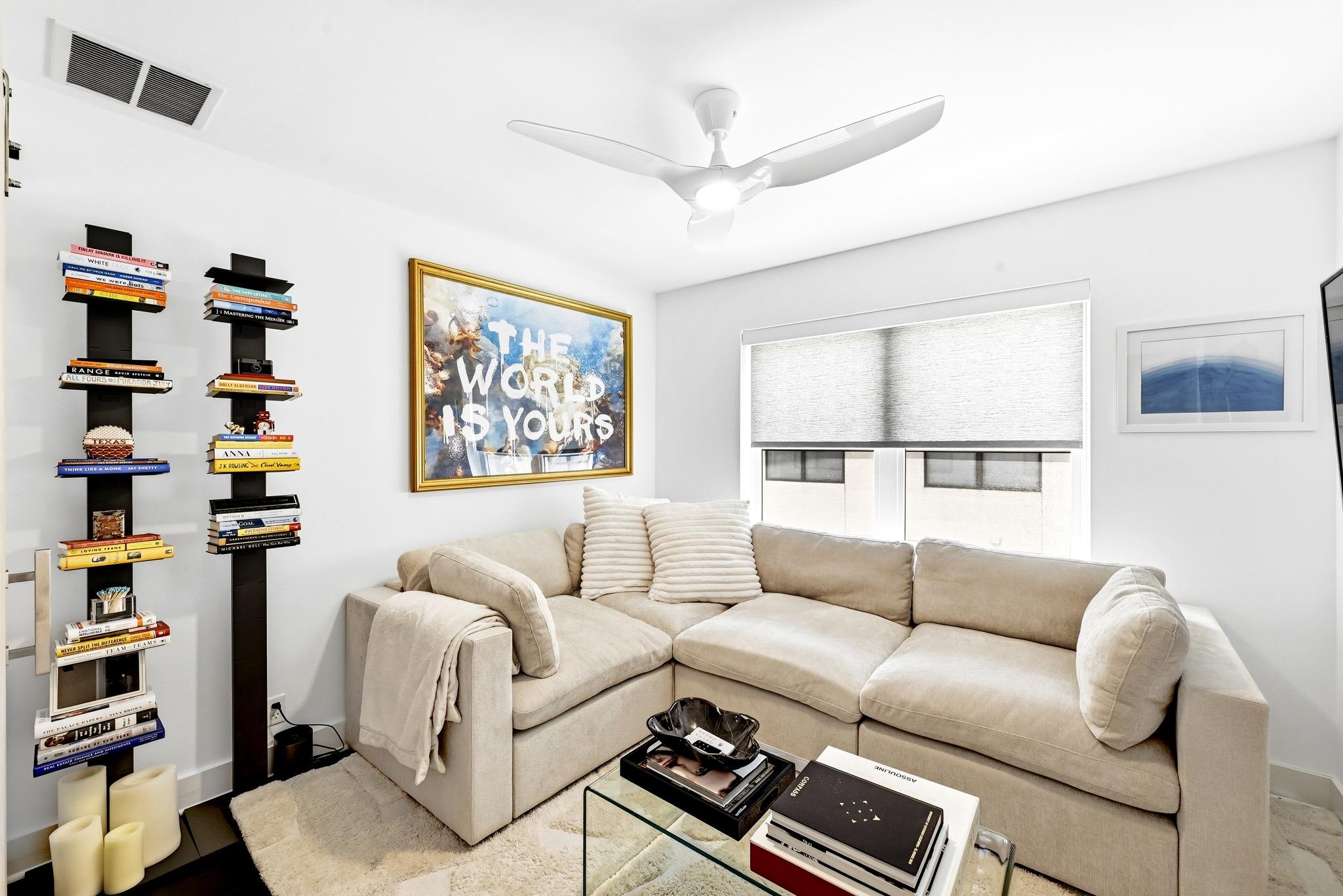 Living room with a beige sectional, tall book displays, and framed “THE WORLD IS YOURS” artwork.