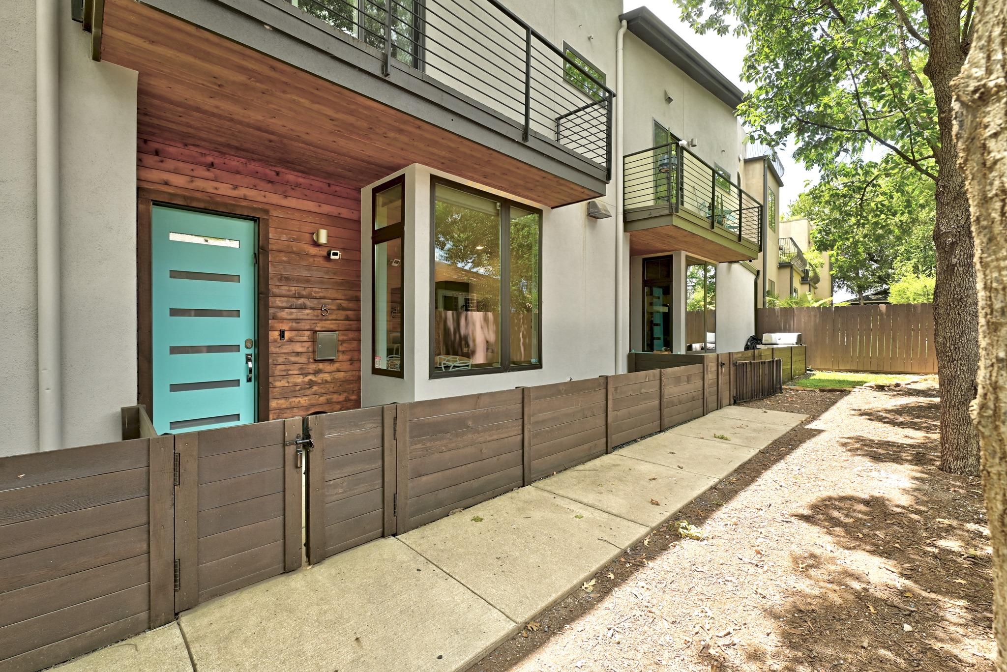 Modern residence with a turquoise entry door, wood siding, metal balconies, and a fenced patio.