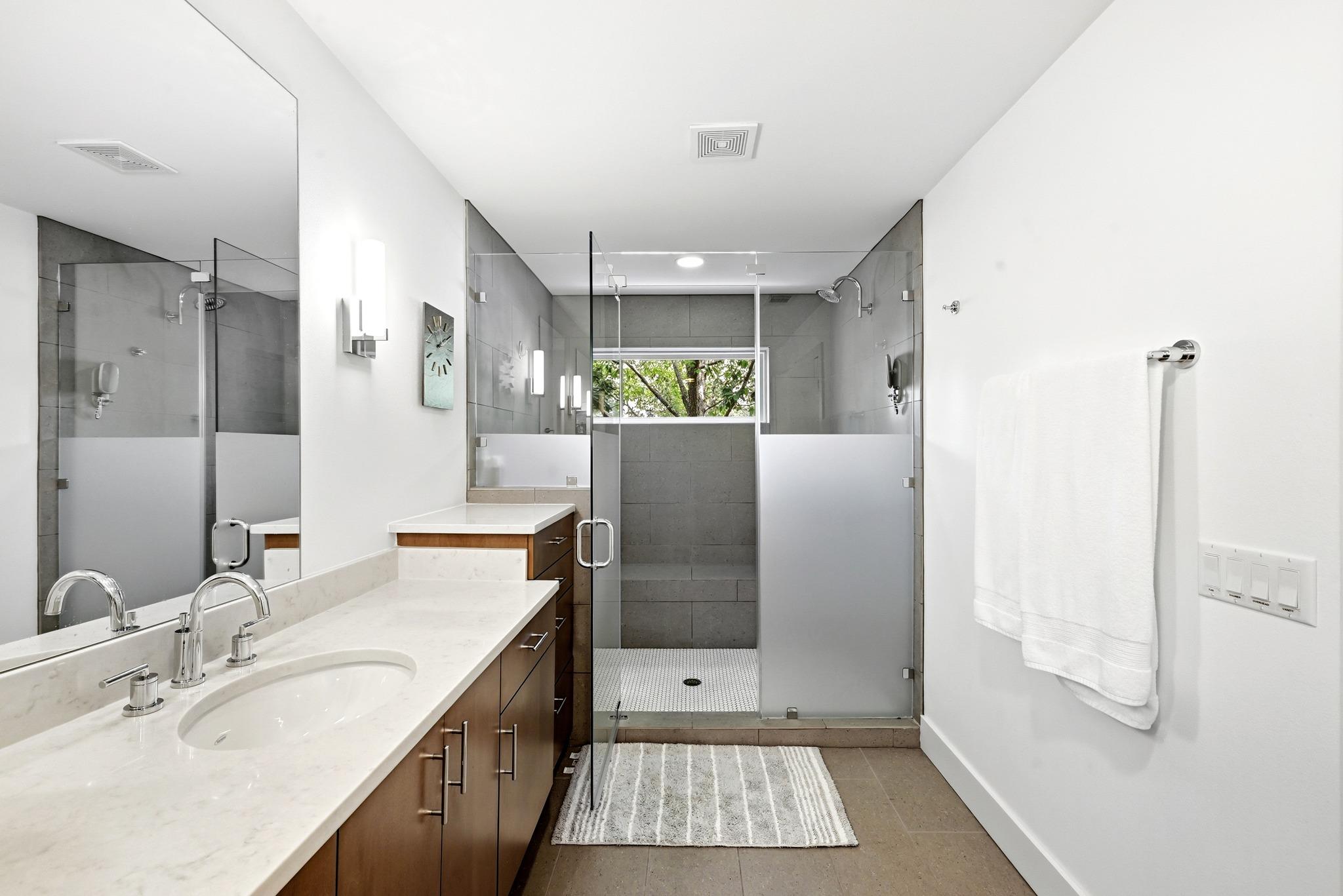 Modern bathroom with a wood double vanity and glass-enclosed gray-tile shower.