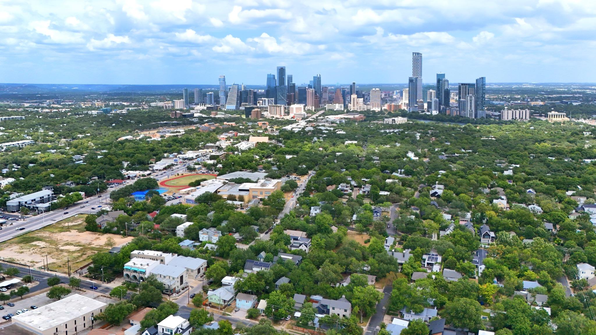 Aerial view across leafy Austin neighborhoods toward the downtown skyline.