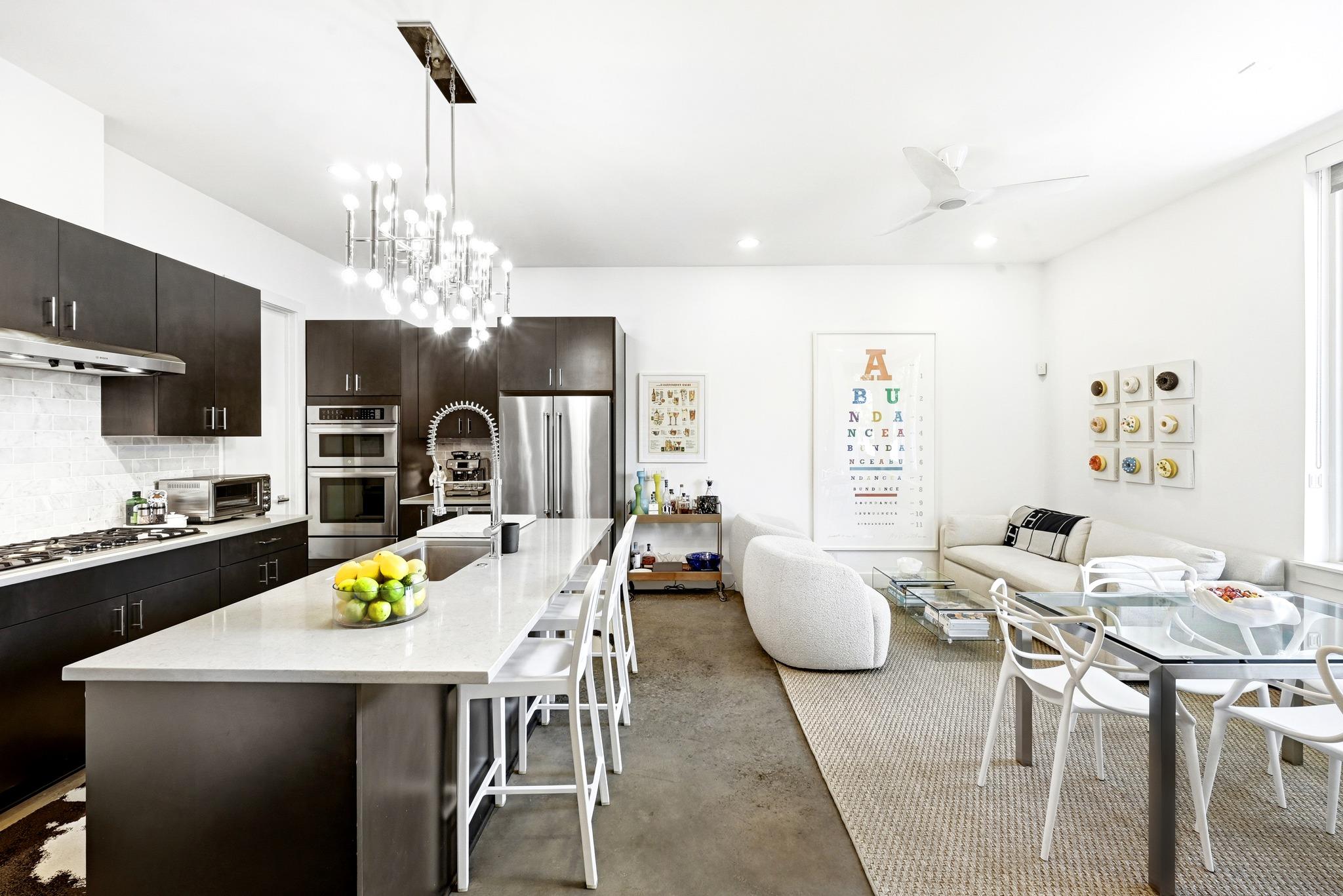 Open-plan kitchen and living room with a white island, dark cabinets, and cream seating.