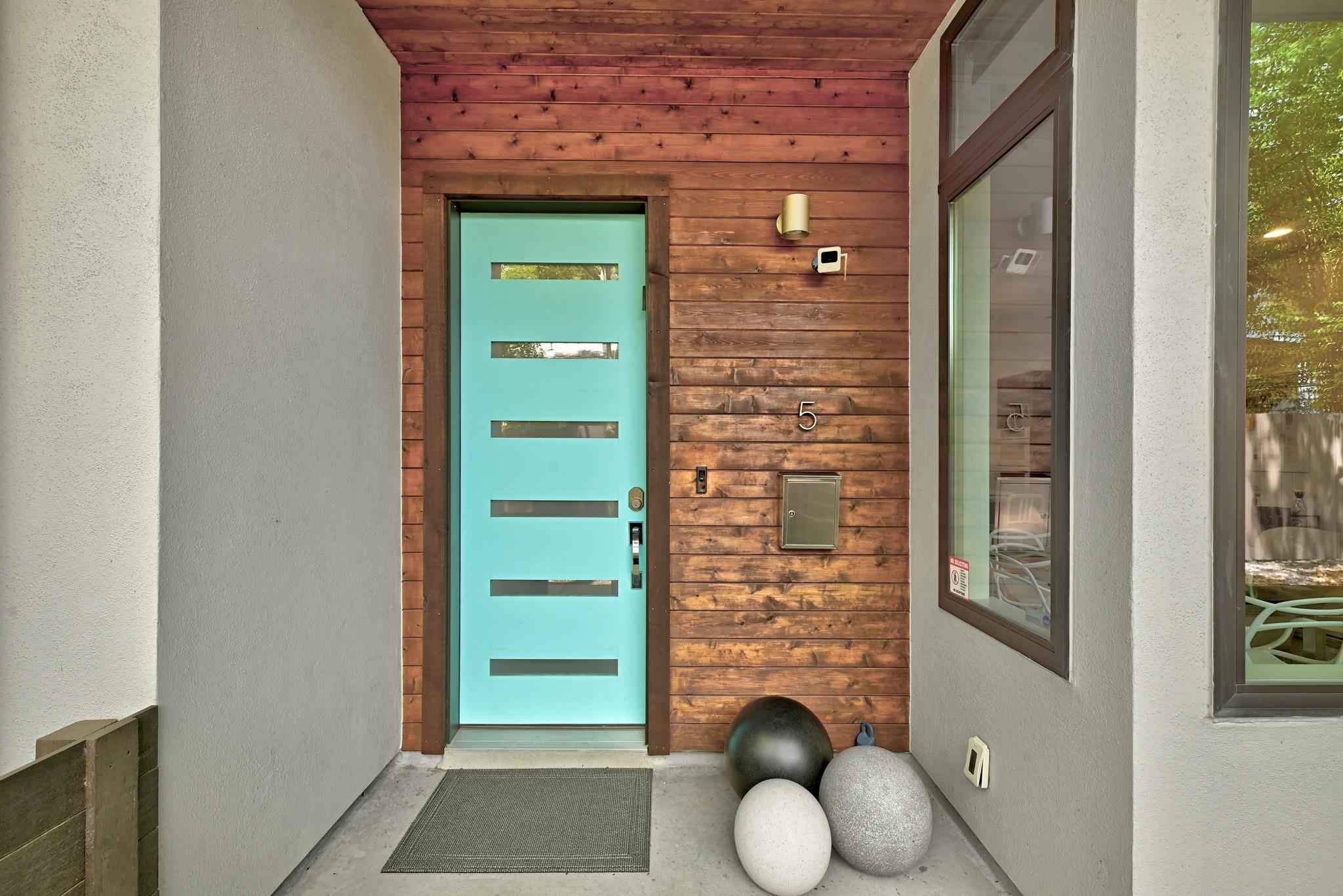 Covered entrance with a turquoise front door, wood-plank siding, and decorative spheres.