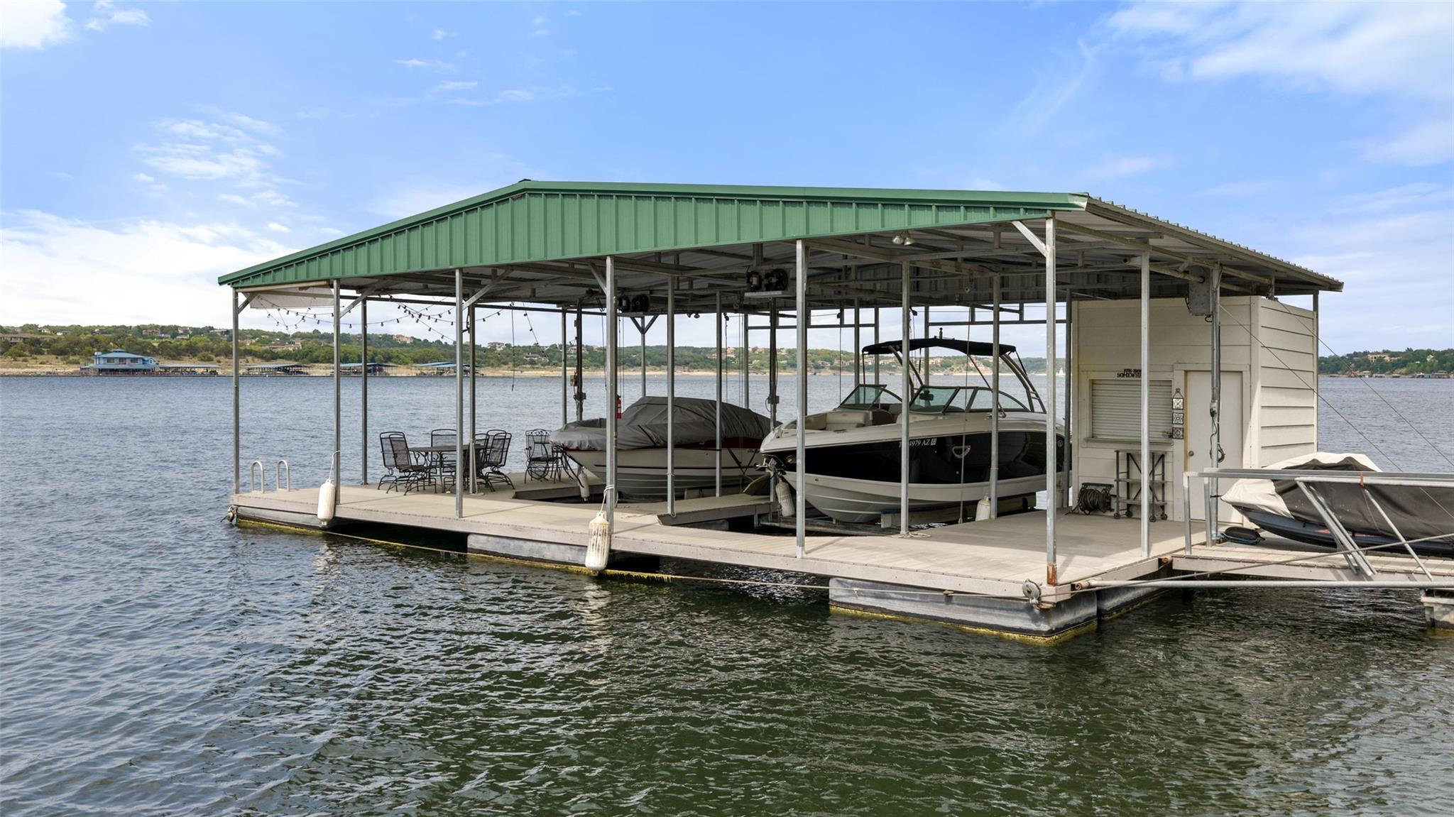 Covered boat dock with a green metal roof and boats on the lake.