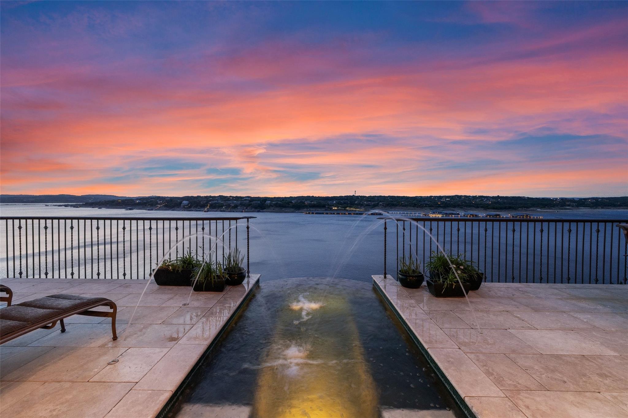 Terrace pool overlooks a lake at dusk beneath a vivid pink and blue sunset.
