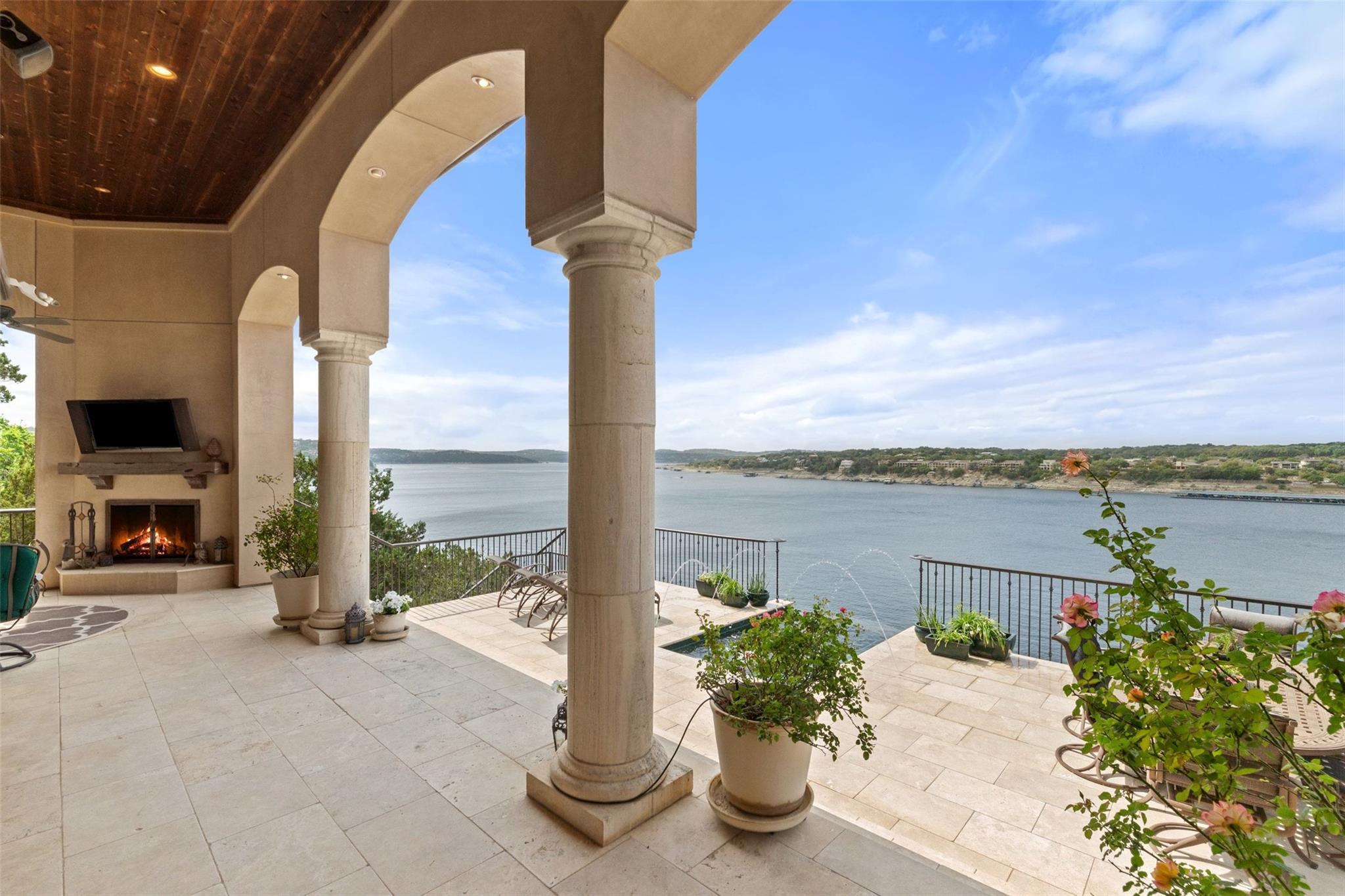 Covered lakeside patio with stone columns, a fireplace, and an expansive water view.