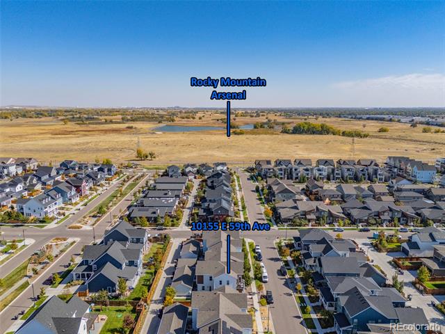 Aerial view of 10155 E 59th Avenue, with neighborhood homes and a broad open field beyond.